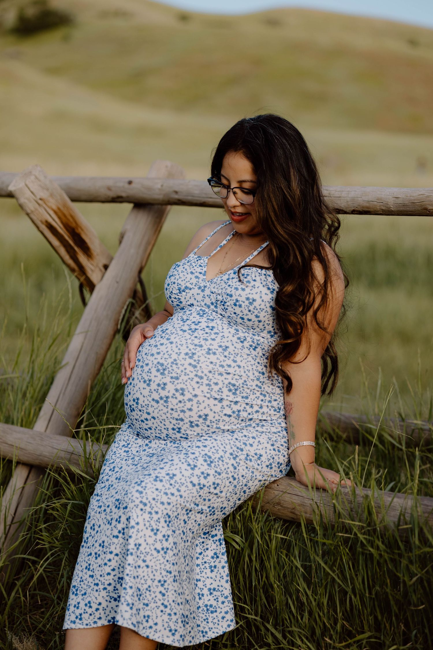 A maternity portrait session against a rustic wooden fence in a natural outdoor setting.