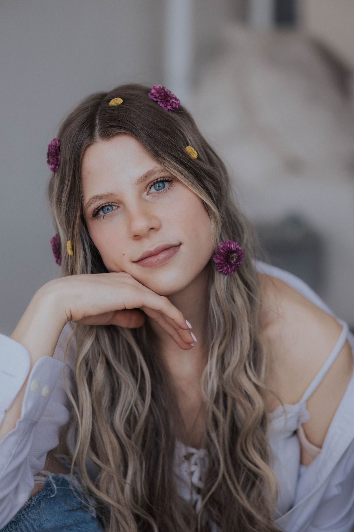 Soft portrait with purple flowers in hair against a neutral background.