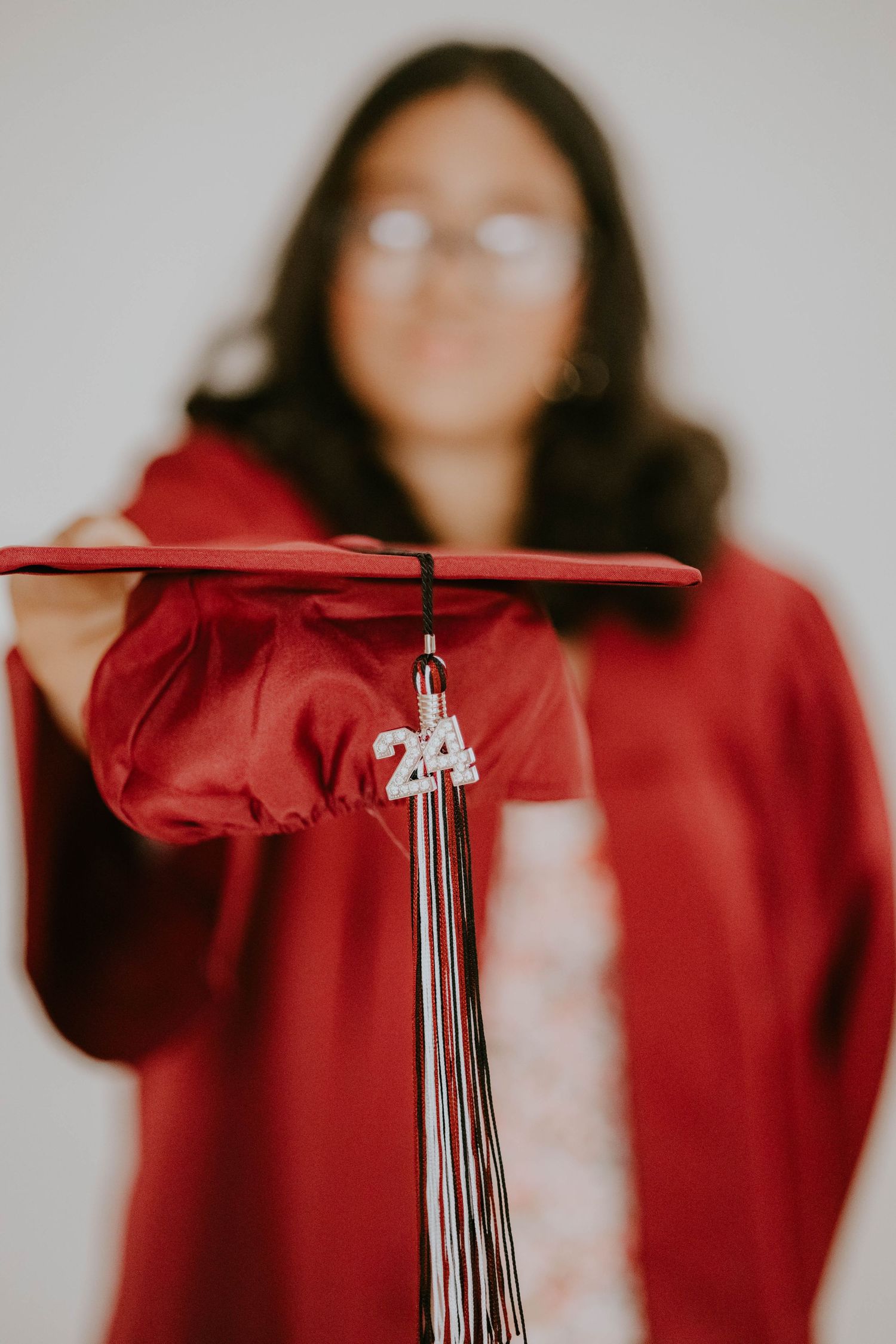 Close-up of graduation cap with silver tassel against red gown background.