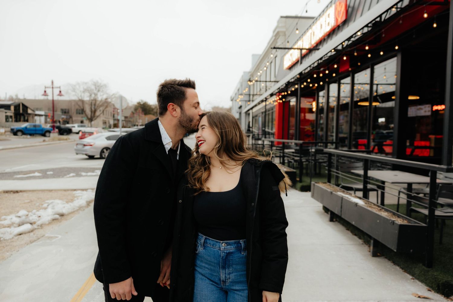 Urban couple photography session outside a storefront with string lights.