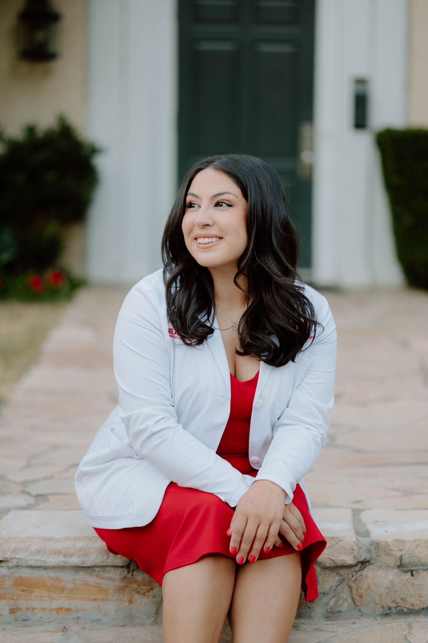 Portrait of woman in red dress and white blazer sitting on stone steps.