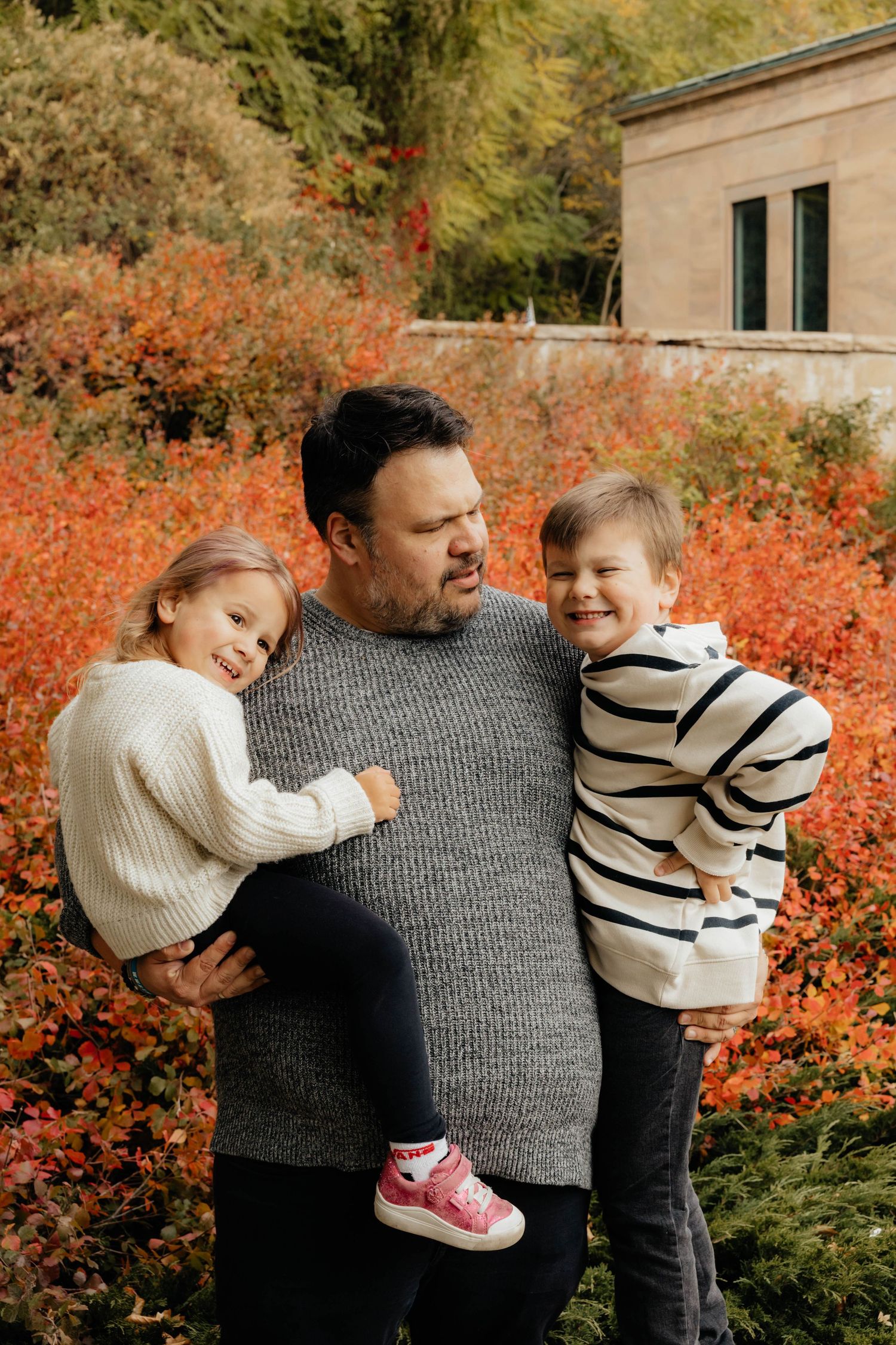 Family enjoying autumn colors together against vibrant red foliage in a candid outdoor photoshoot.