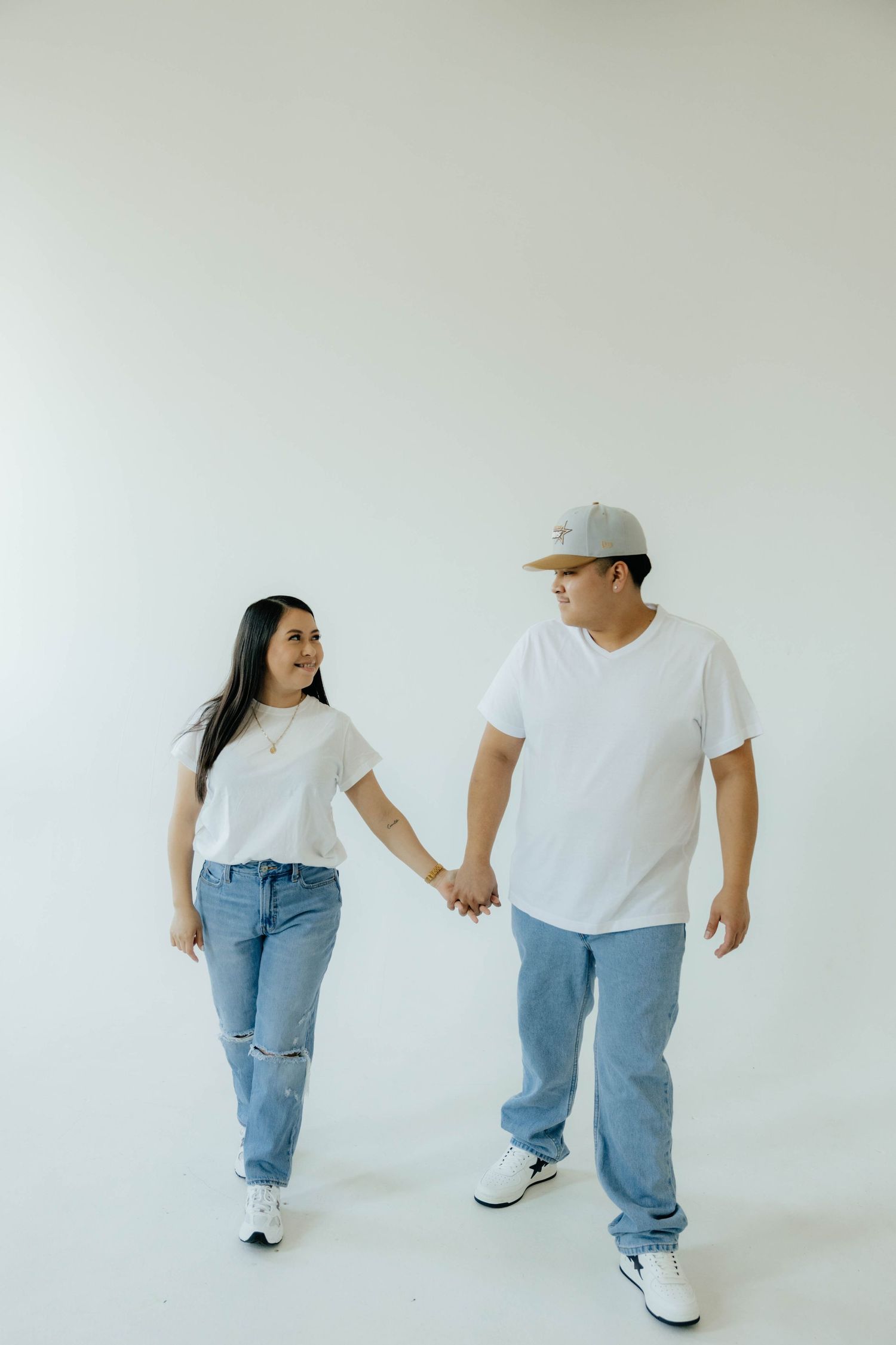 Couple in casual white tops and jeans walking playfully against a minimalist background.