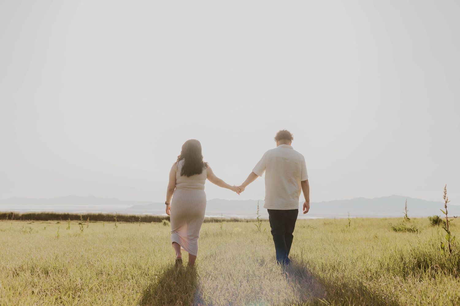 Couple walking hand in hand through golden meadow at sunset.