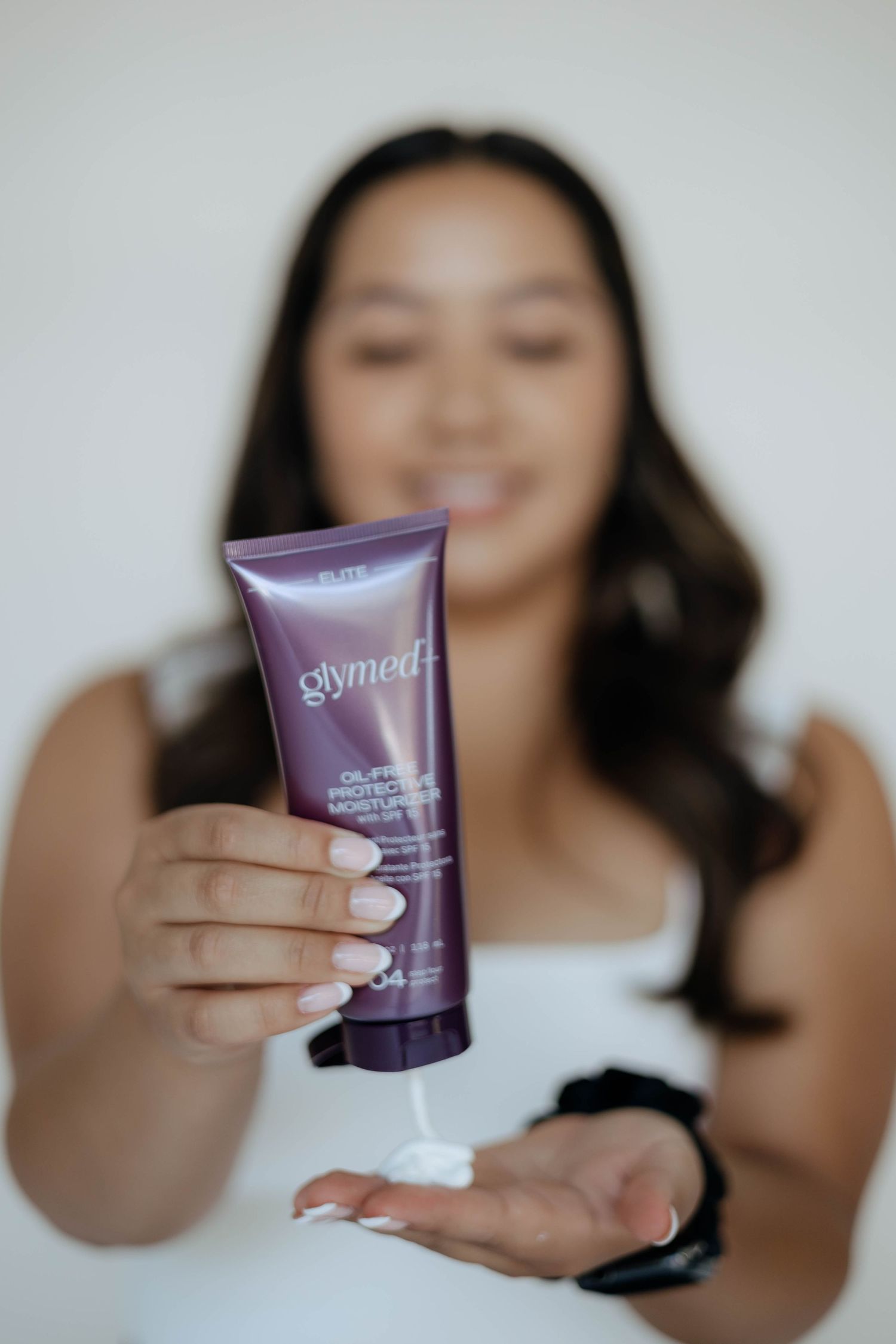 Person displaying purple skincare product container against white background.
