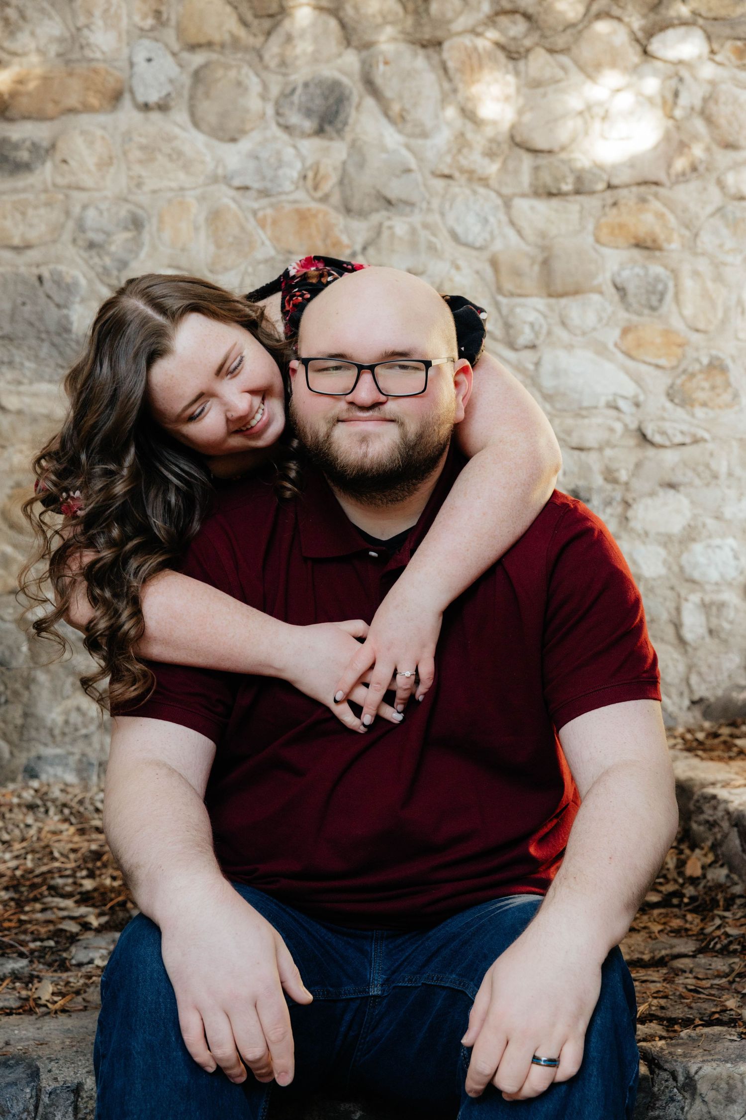 Affectionate couple posing against a rustic stone wall background.