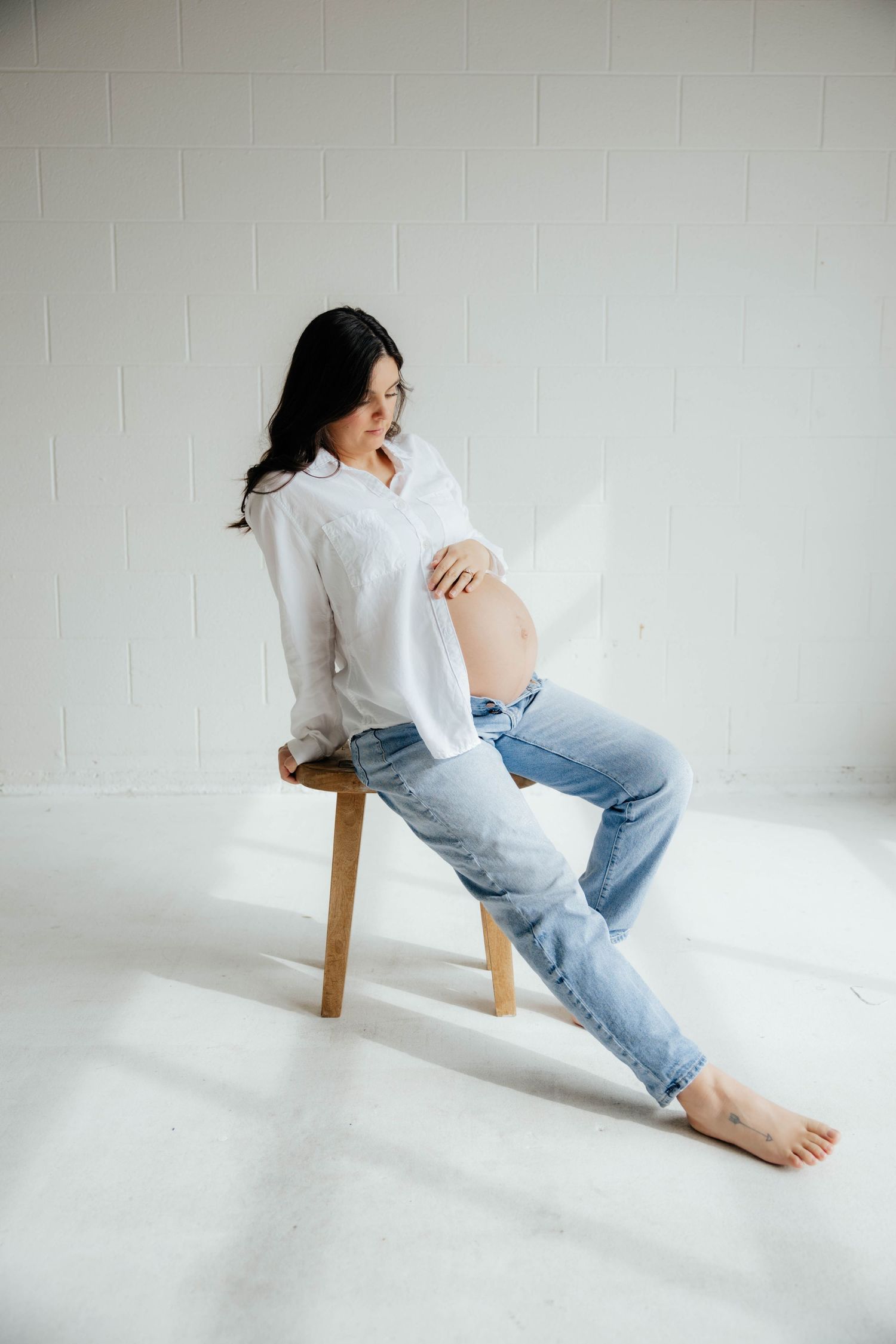 Casual portrait of person in white shirt and jeans sitting sideways on wooden stool.