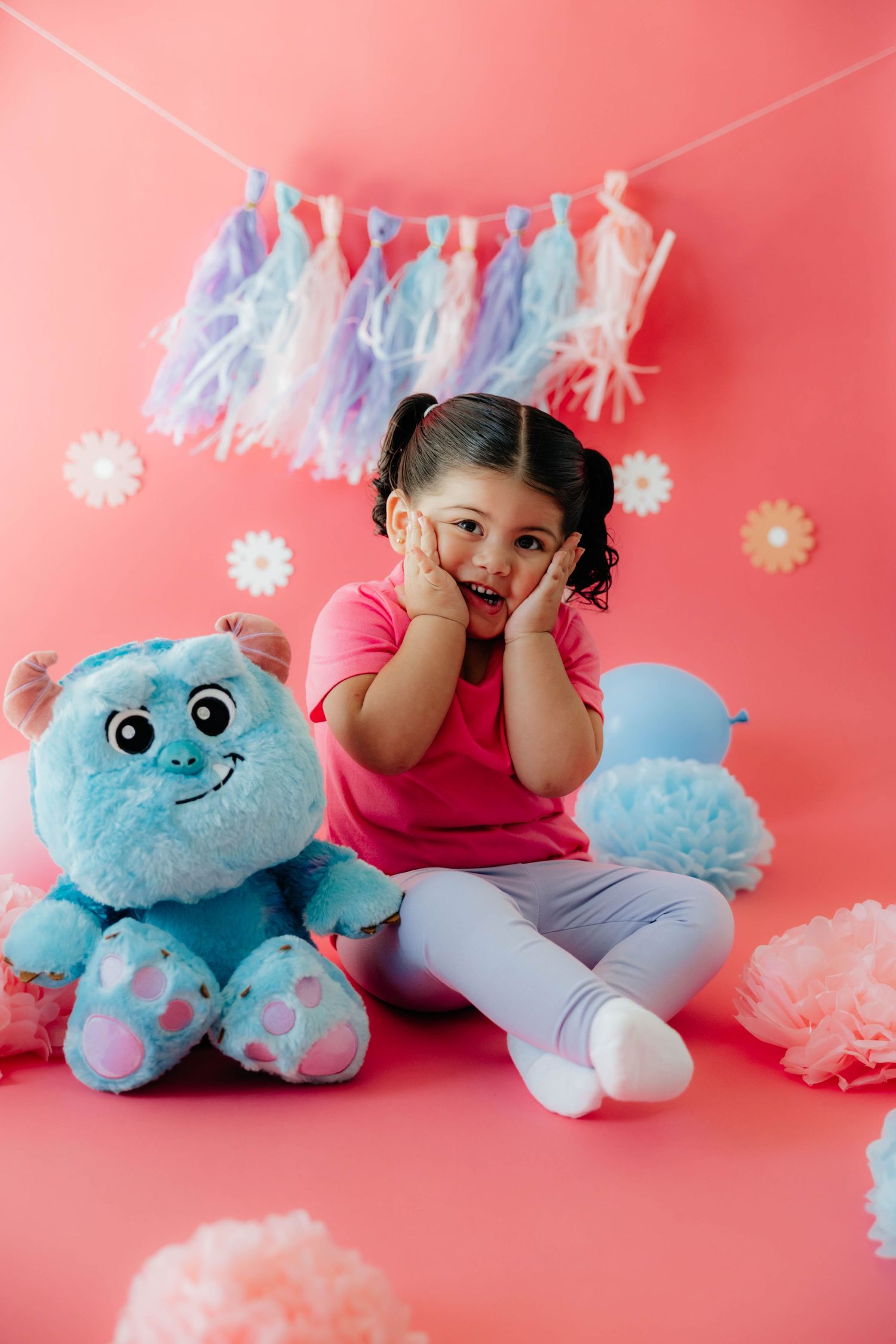 Playful scene with blue plush toy and festive pastel decorations against pink background.