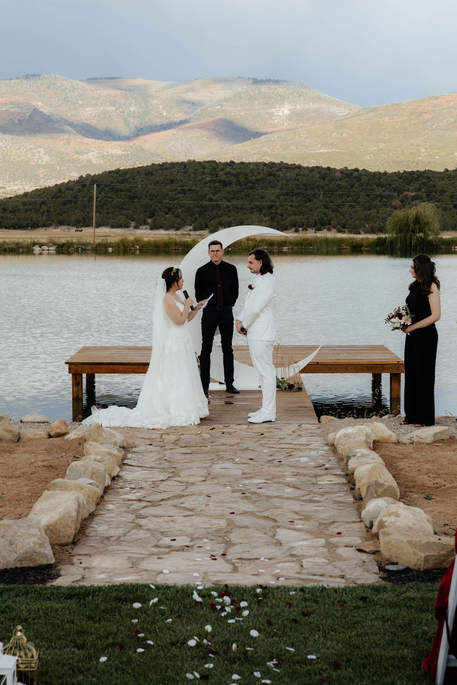 Lakeside wedding ceremony on stone dock with mountains in background.