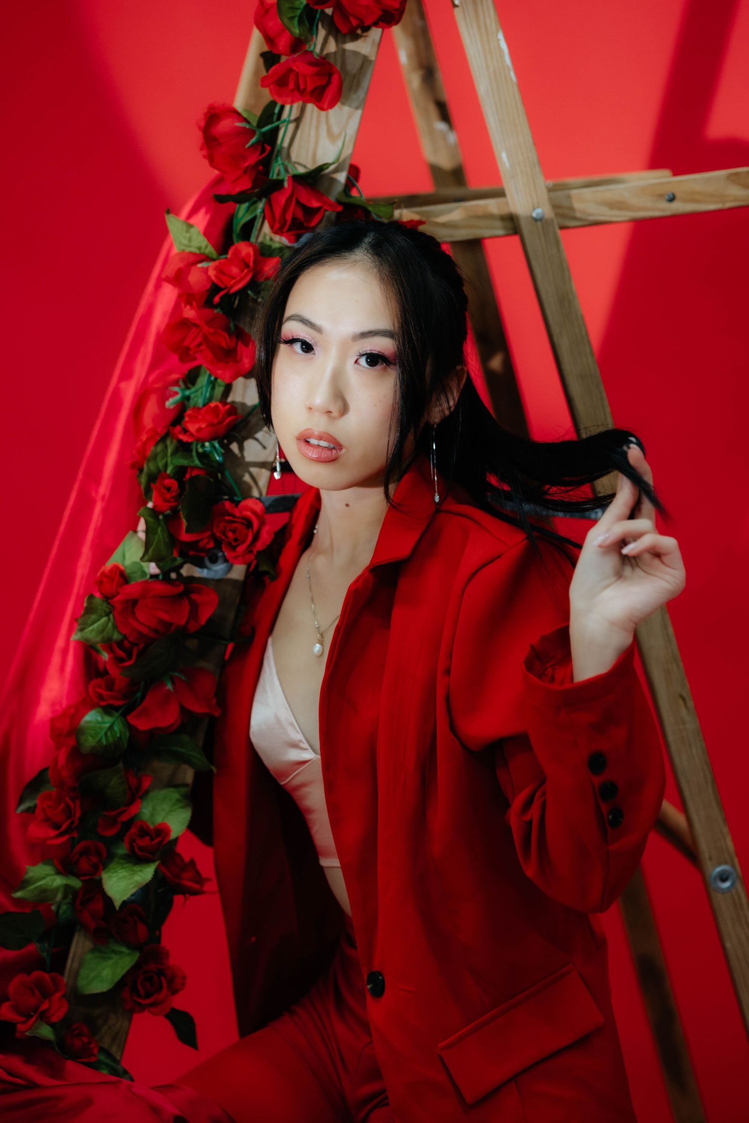 Dramatic portrait series with red roses and wooden ladder against vibrant red background.