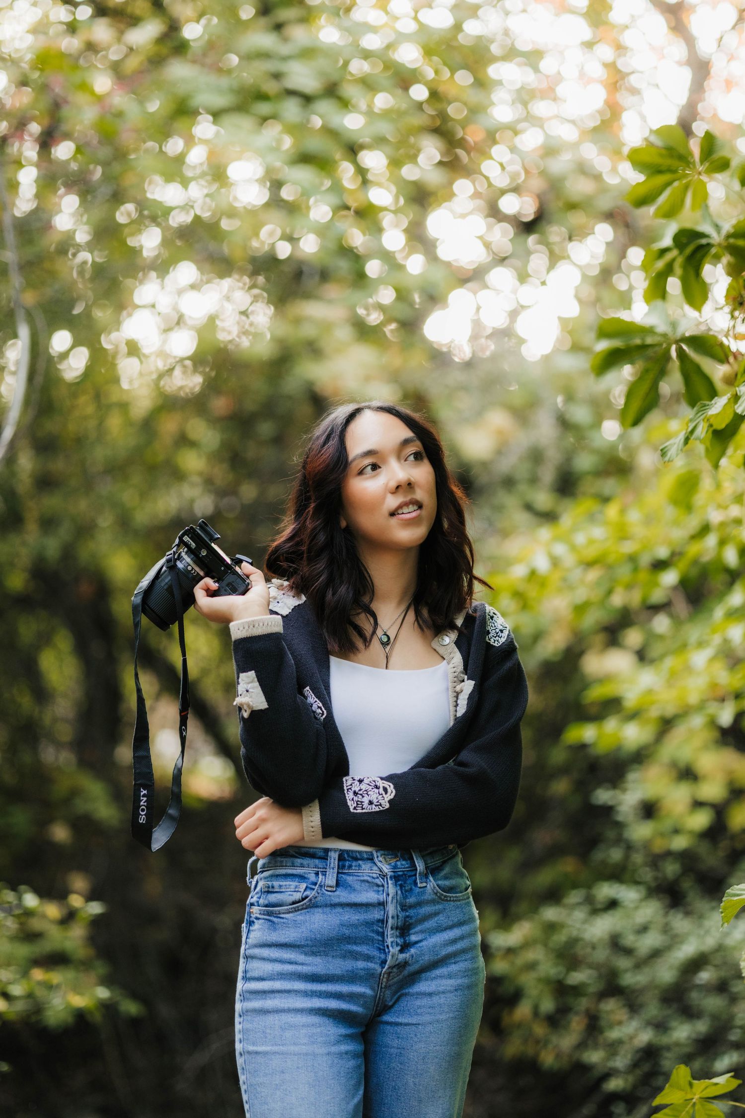 Photographer in casual outfit holds camera in outdoor nature setting.