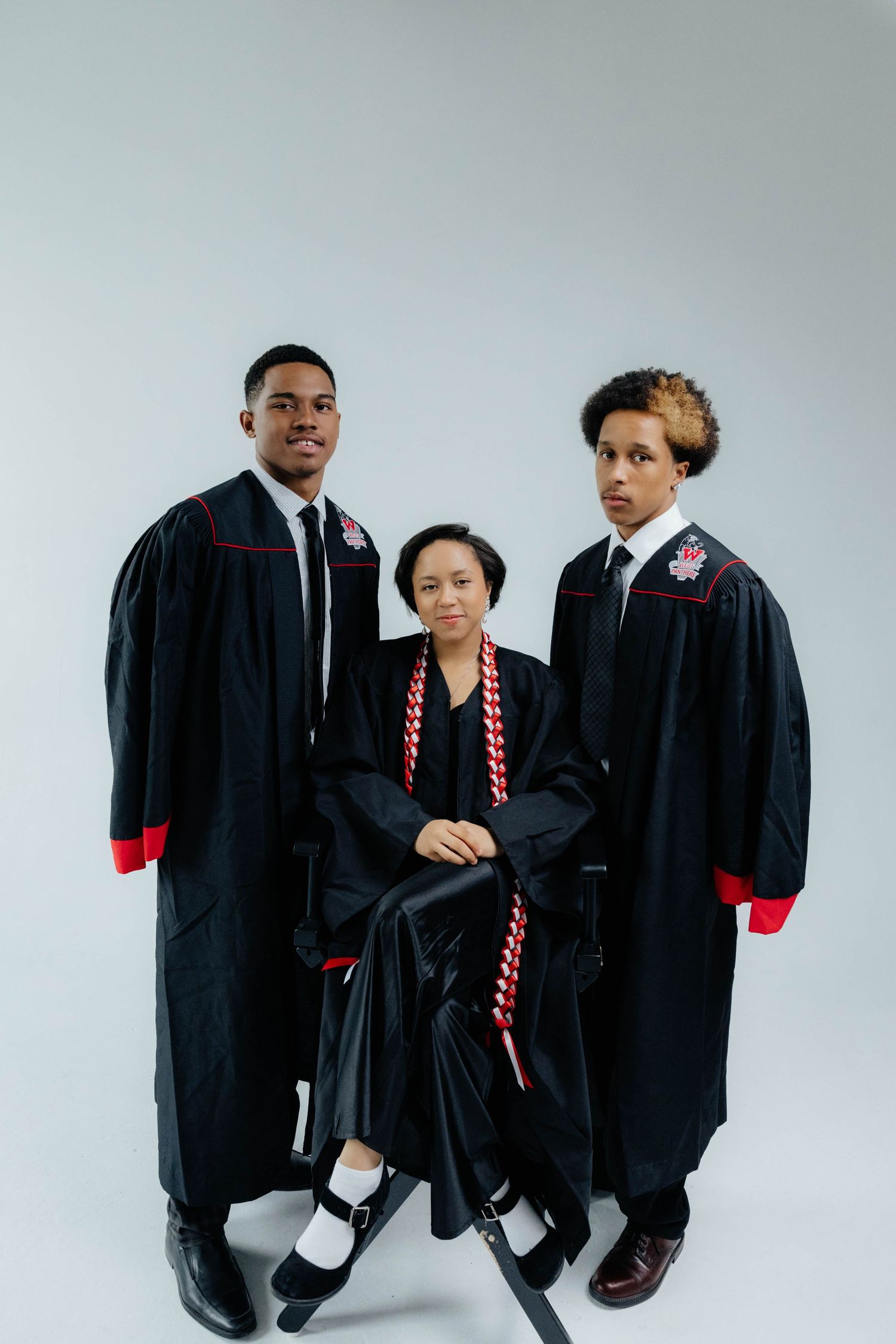 Group photo of graduates in black academic robes with red accents posing against white background.