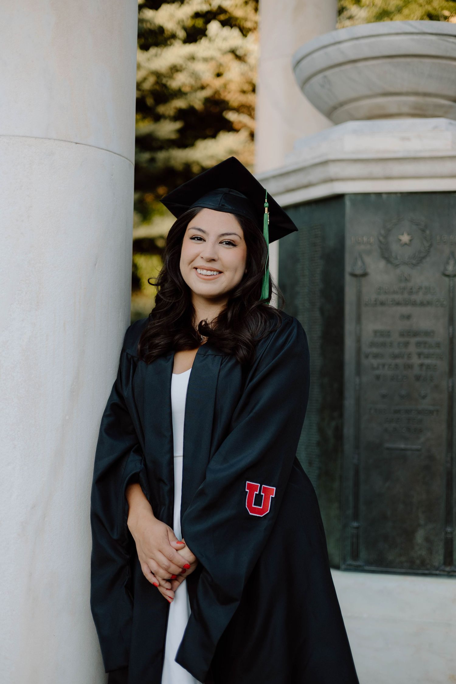 Graduate in cap and gown poses elegantly between white columns during graduation photoshoot.