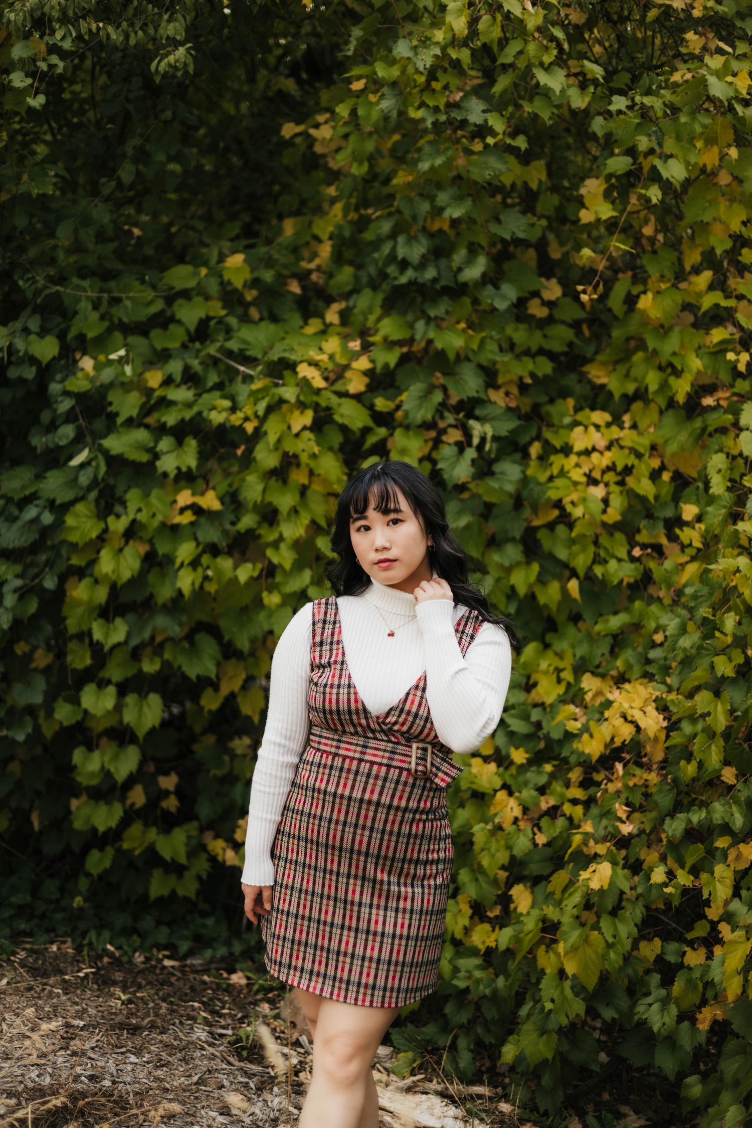 Autumn portrait session against yellow-green foliage wearing plaid dress.