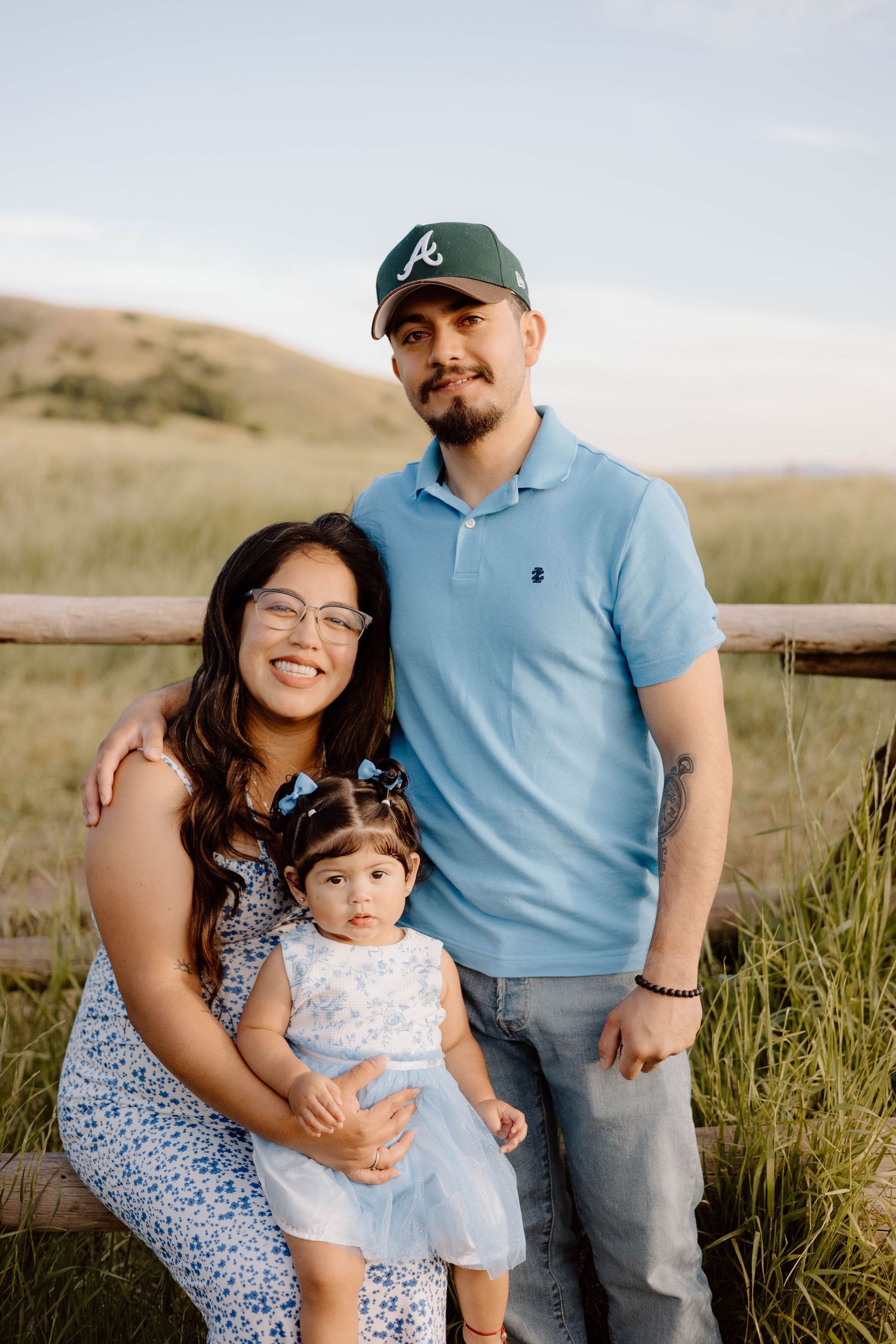 Family portrait session in a grassy field with wooden fence backdrop.