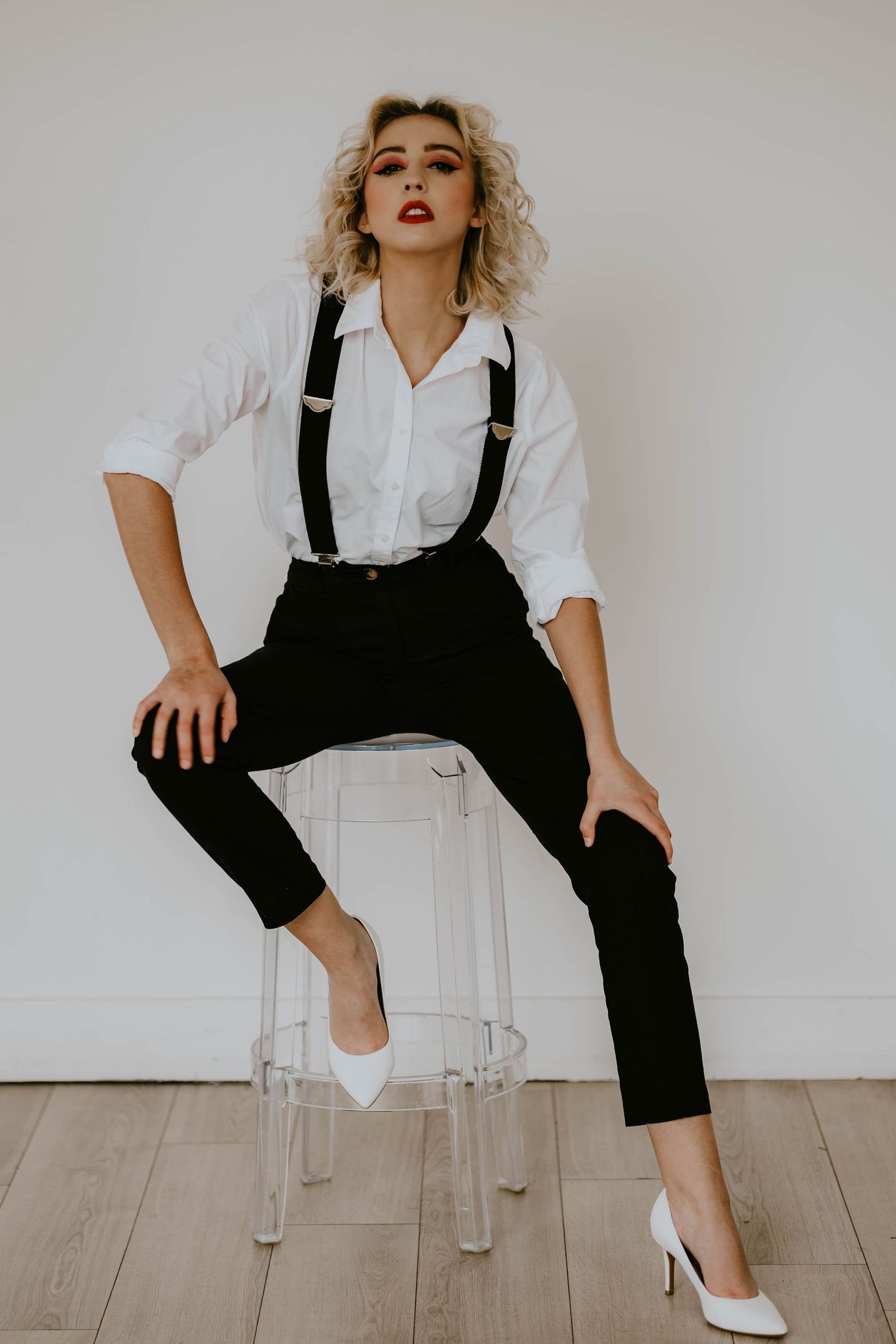 Fashion portrait in white shirt and black suspenders sitting on clear chair.