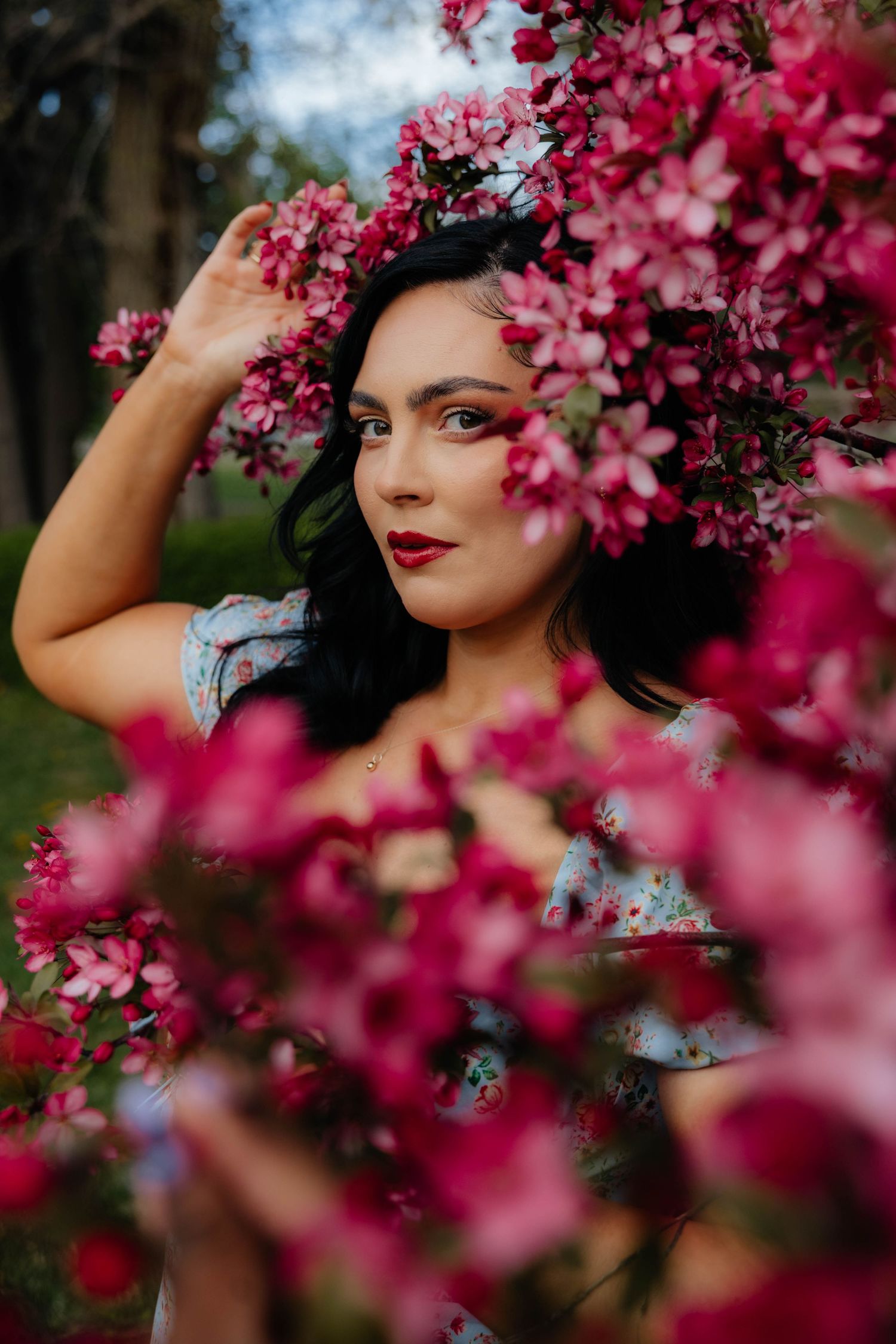 Artistic portrait through vibrant pink cherry blossoms with soft bokeh effect.