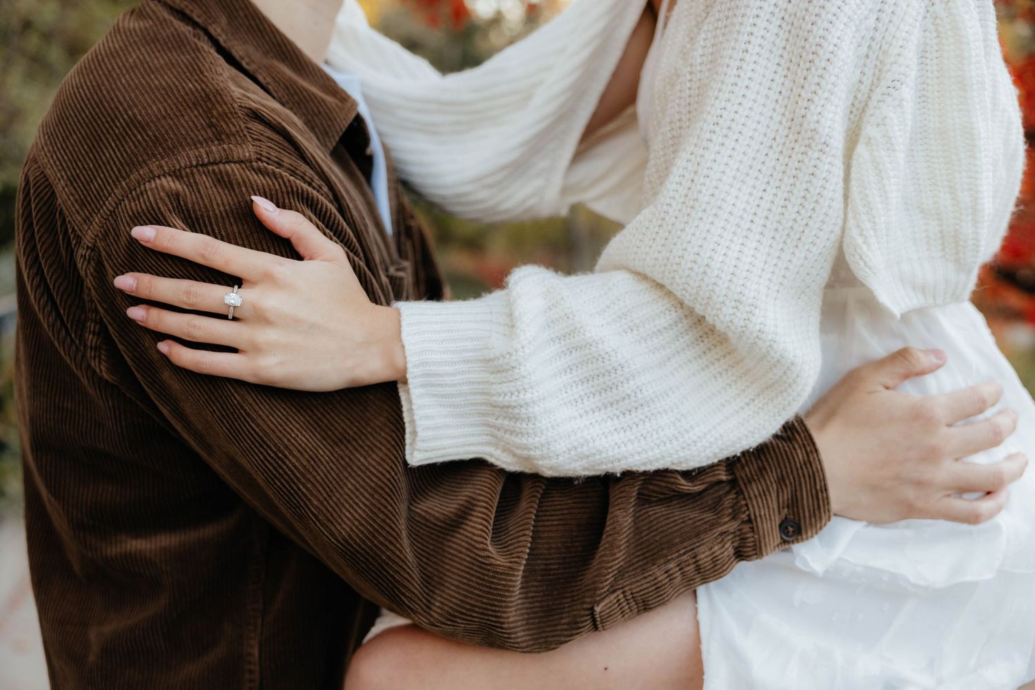 Intimate embrace showing white sweater and brown jacket in natural lighting.