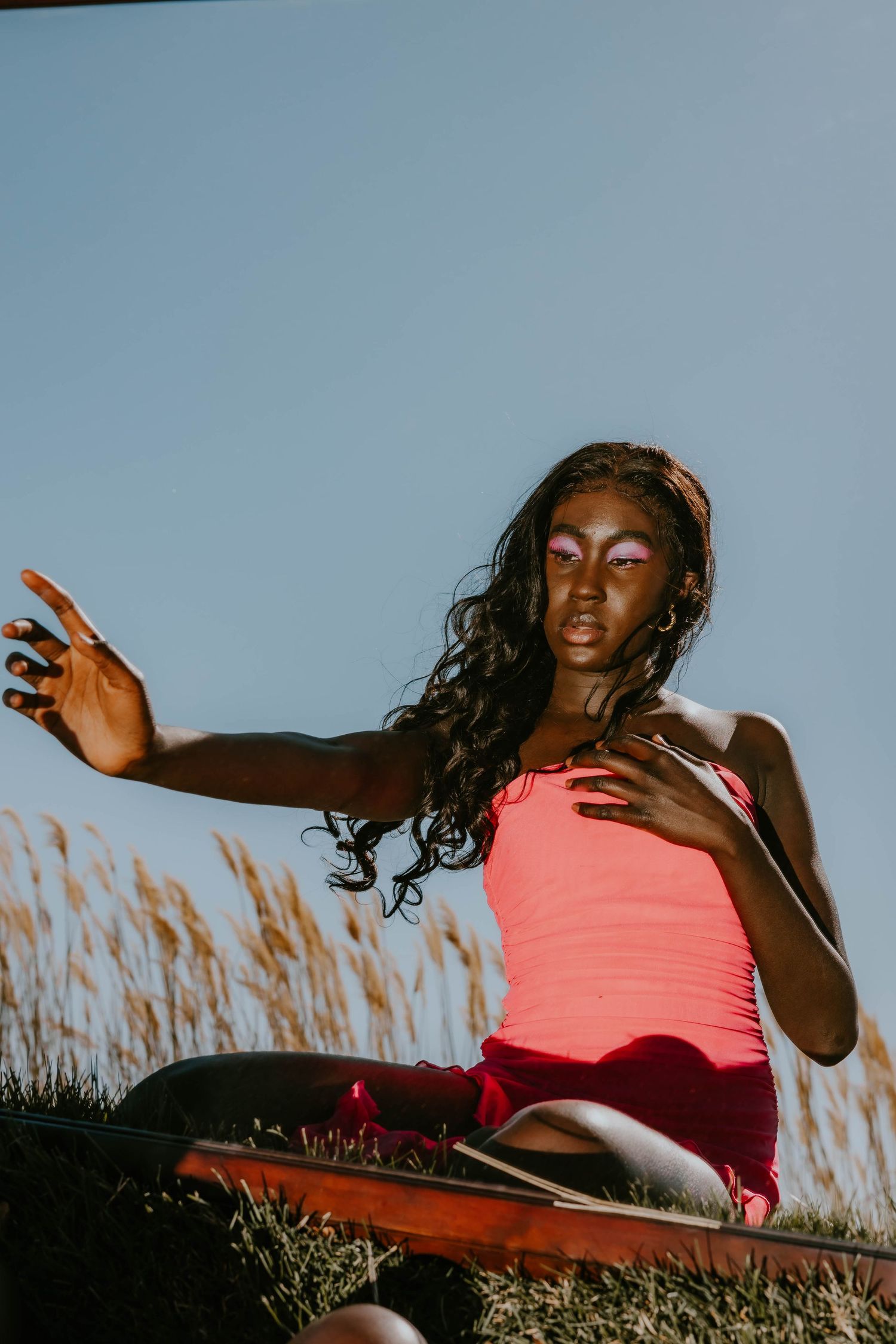 Artistic outdoor photoshoot in coral top with dramatic lighting and grass backdrop.