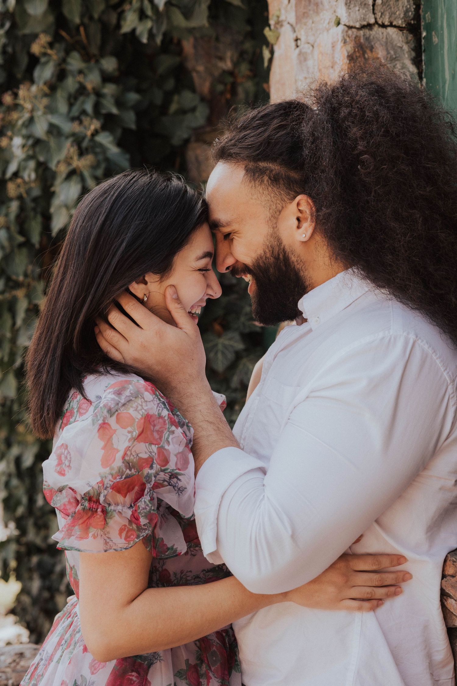 Couple sharing an intimate moment against a textured wall with ivy.