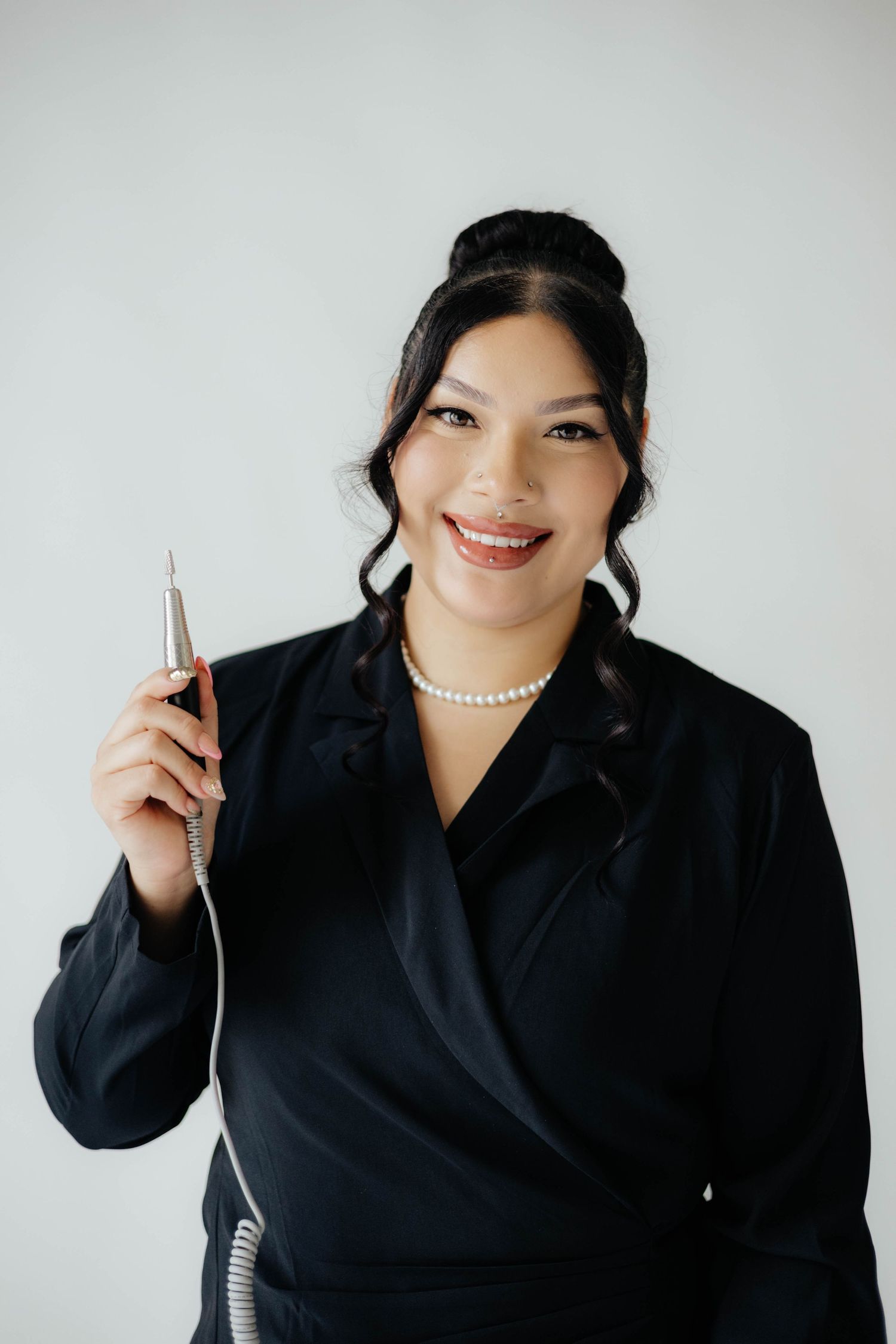 Professional in black blazer and pearl necklace holds pen against white background.