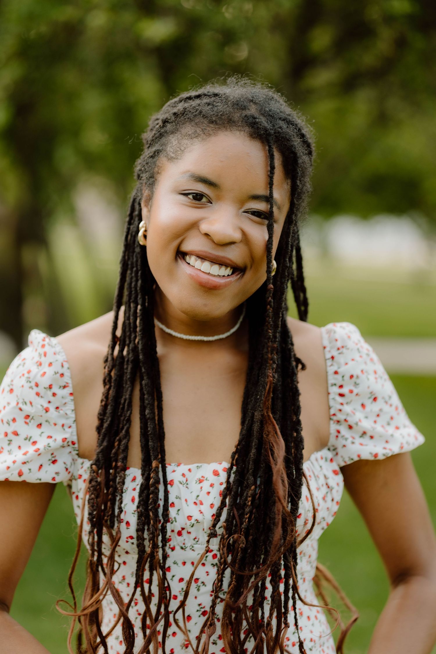 Summer portrait featuring long braids and floral dress in an outdoor garden setting.