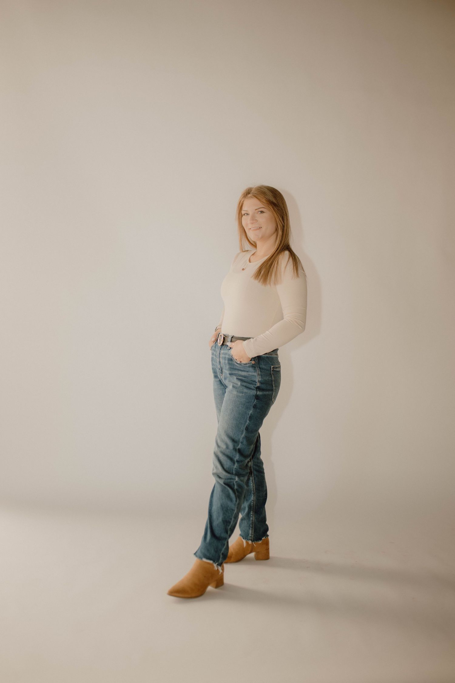 Female photographer Kaitlyn Heslep standing in a studio wearing jeans and blazer, posing casually