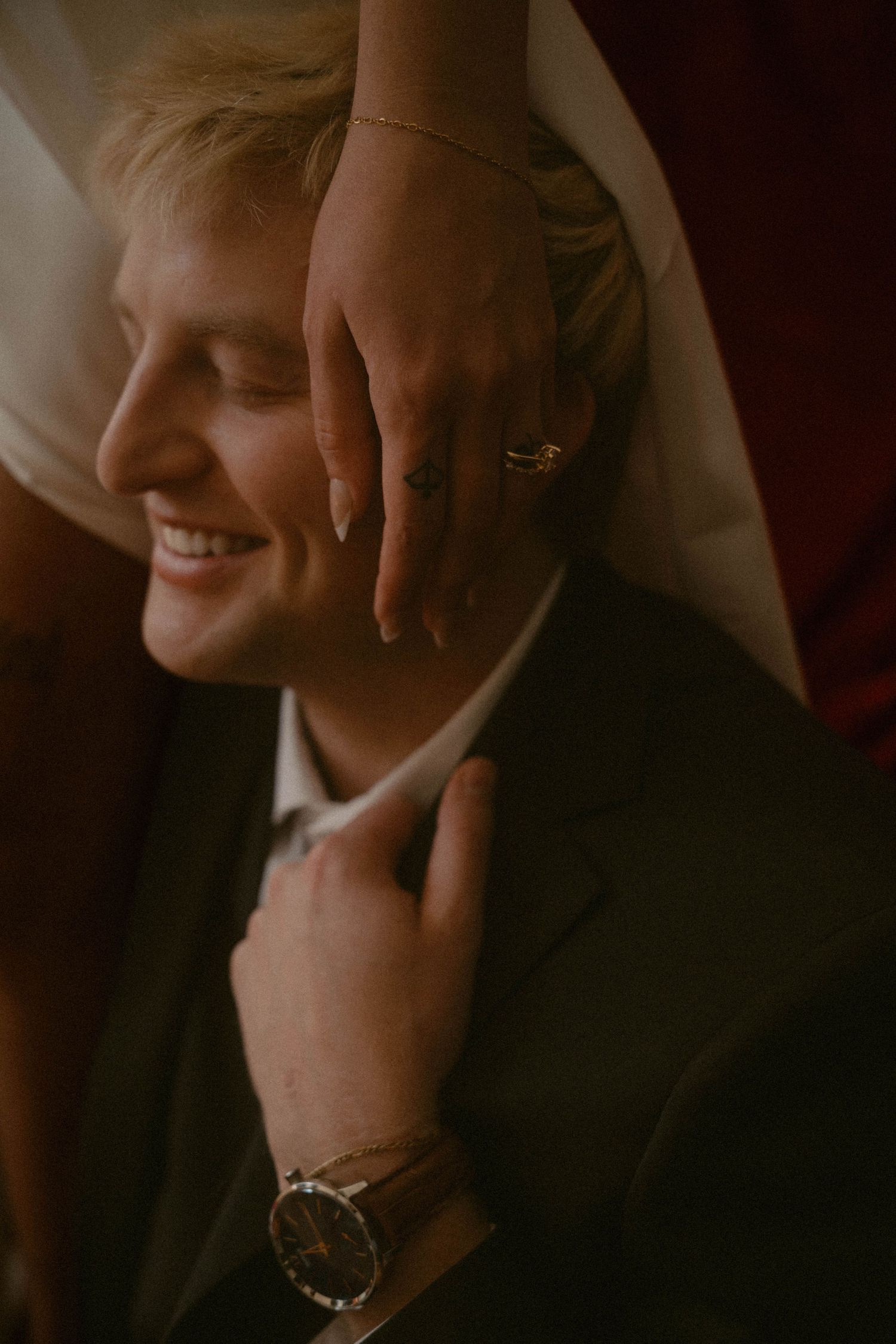 Bride’s hand resting on groom’s face as he smiles in a suit