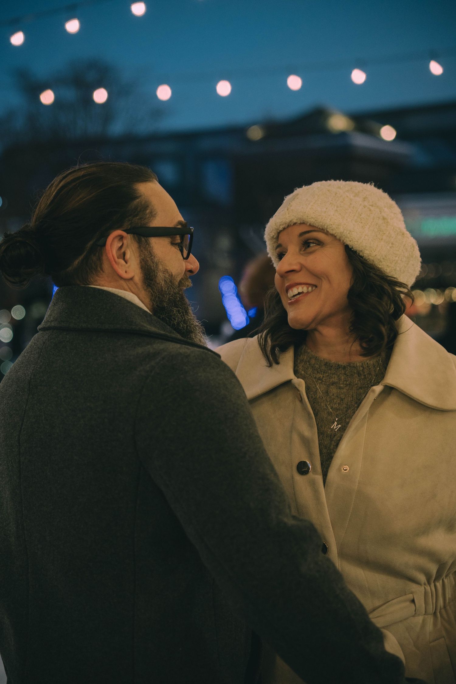 Couple smiling at each other under string lights in the evening