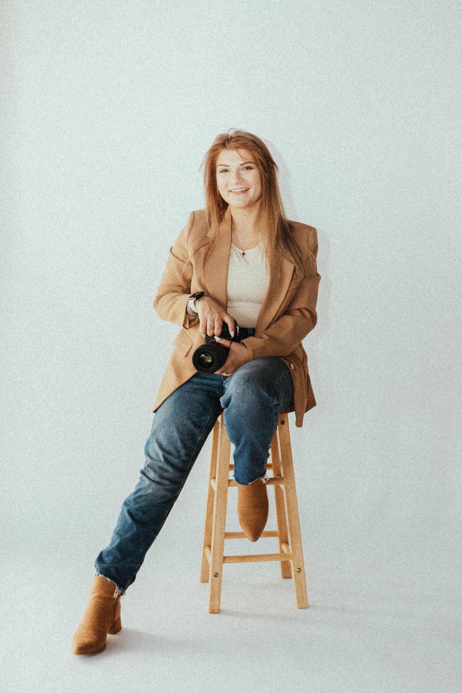 Female photographer Kaitlyn Heslep sitting on a stool holding a camera in a minimal studio setting