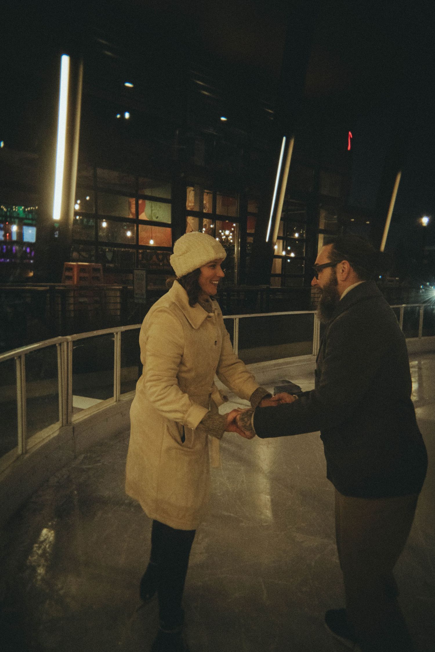 Couple holding hands while ice skating at night in a city setting