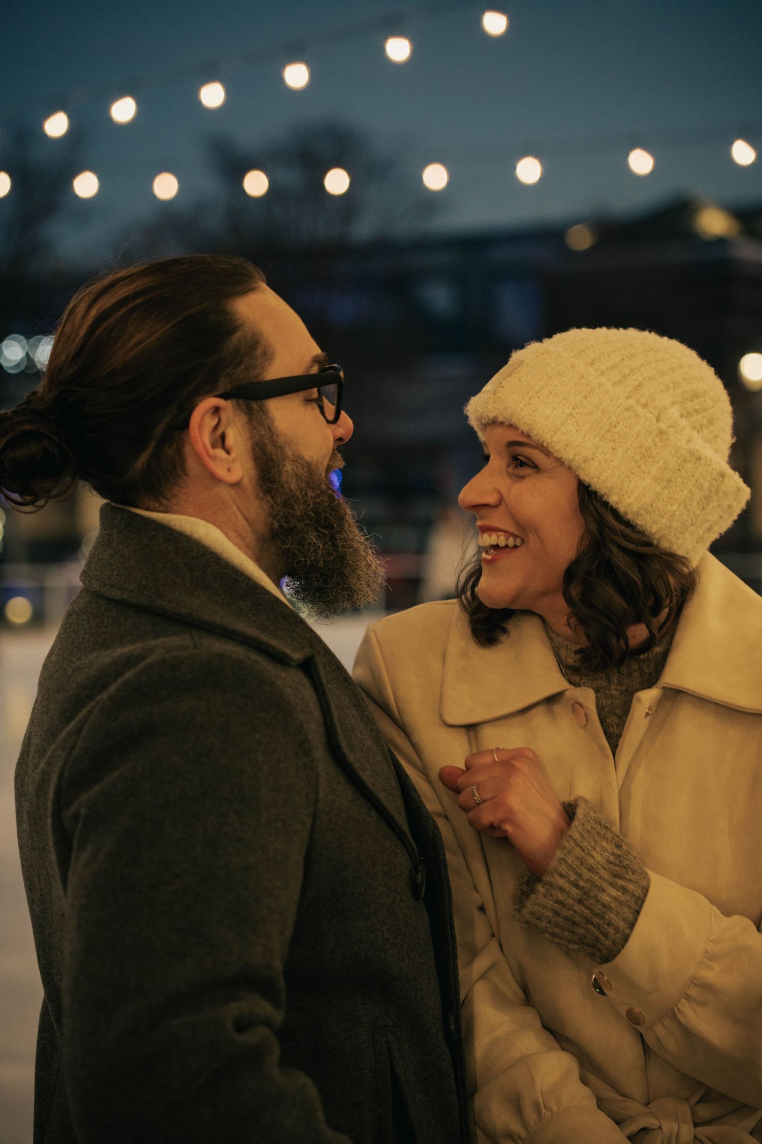 Couple laughing together under string lights during a night outing