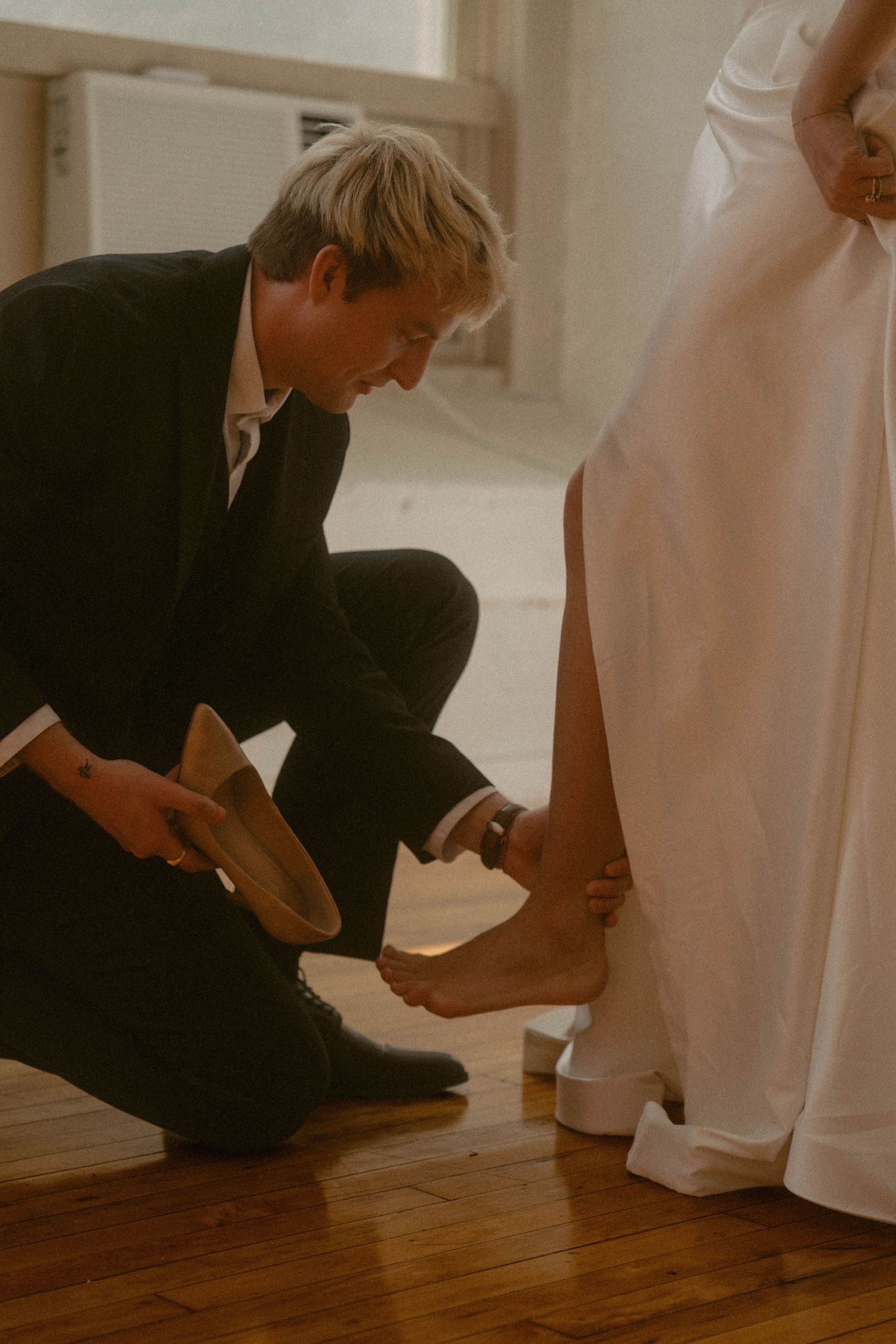 Groom kneeling to help bride put on her shoe during wedding preparation