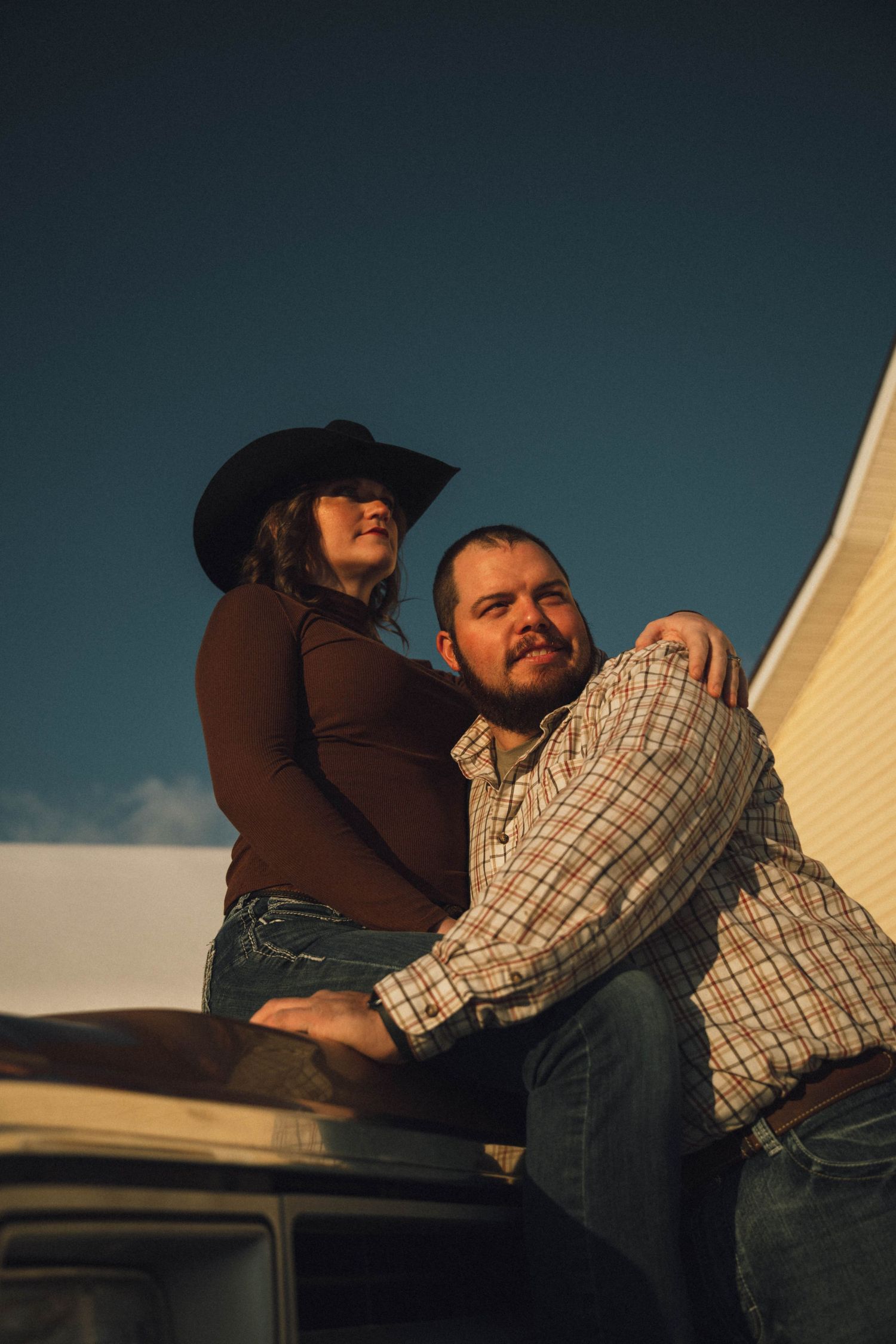 Couple posing on a vintage truck in warm golden light wearing western attire