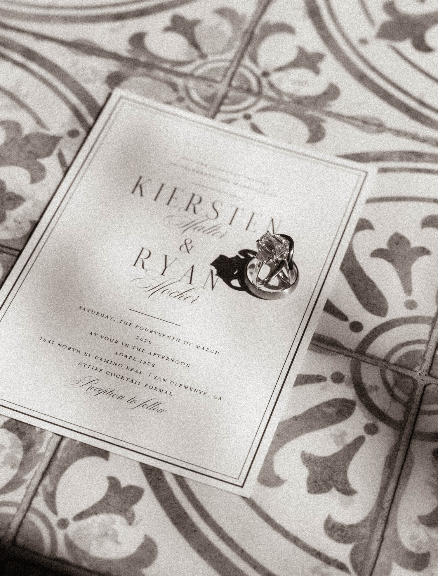 Black and white wedding invitation for Kiersten and Ryan with elegant typography, diamond ring on ornate tile background.