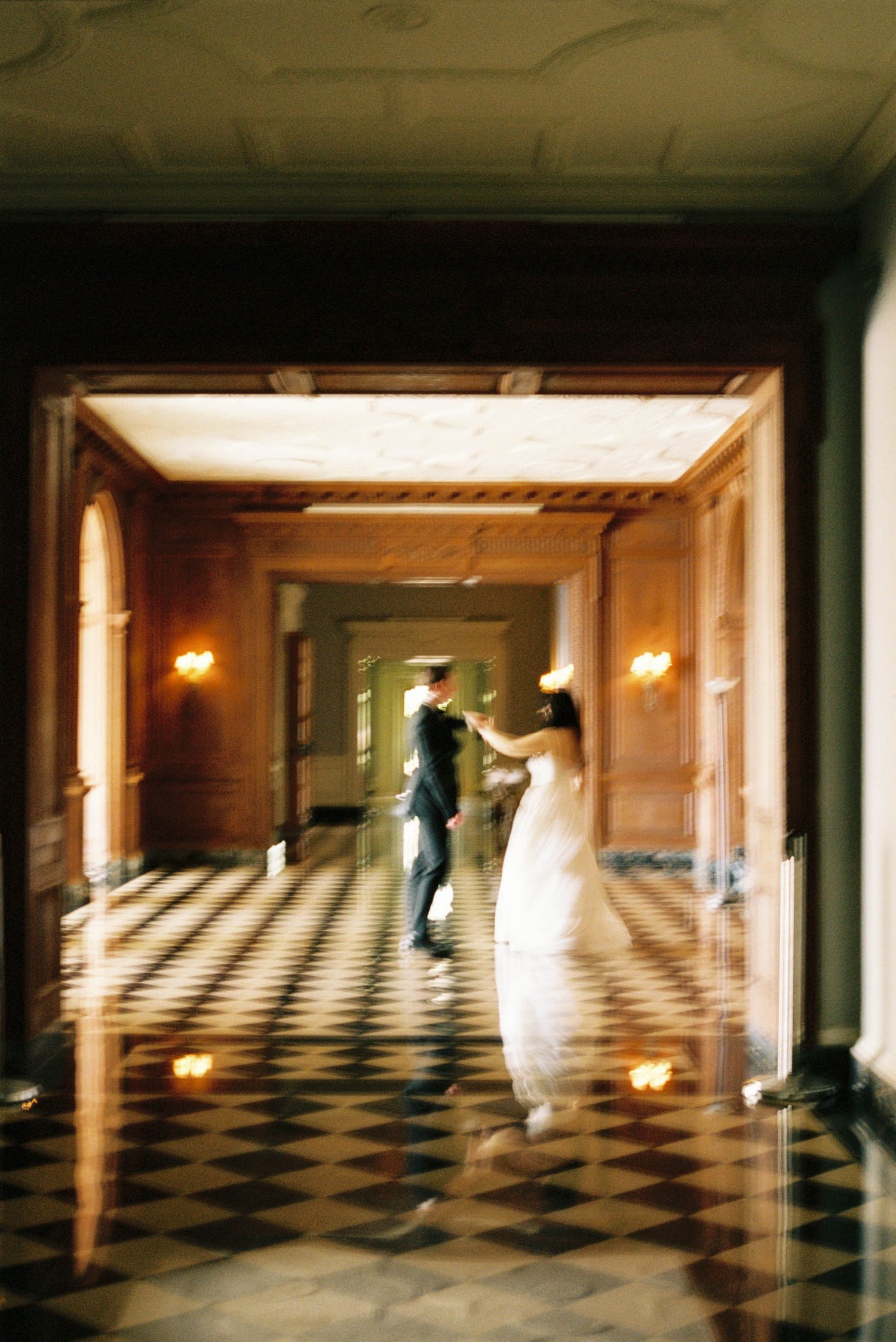Bride and groom dancing in an elegant hallway with checkered floors and warm candlelight at a wedding venue.