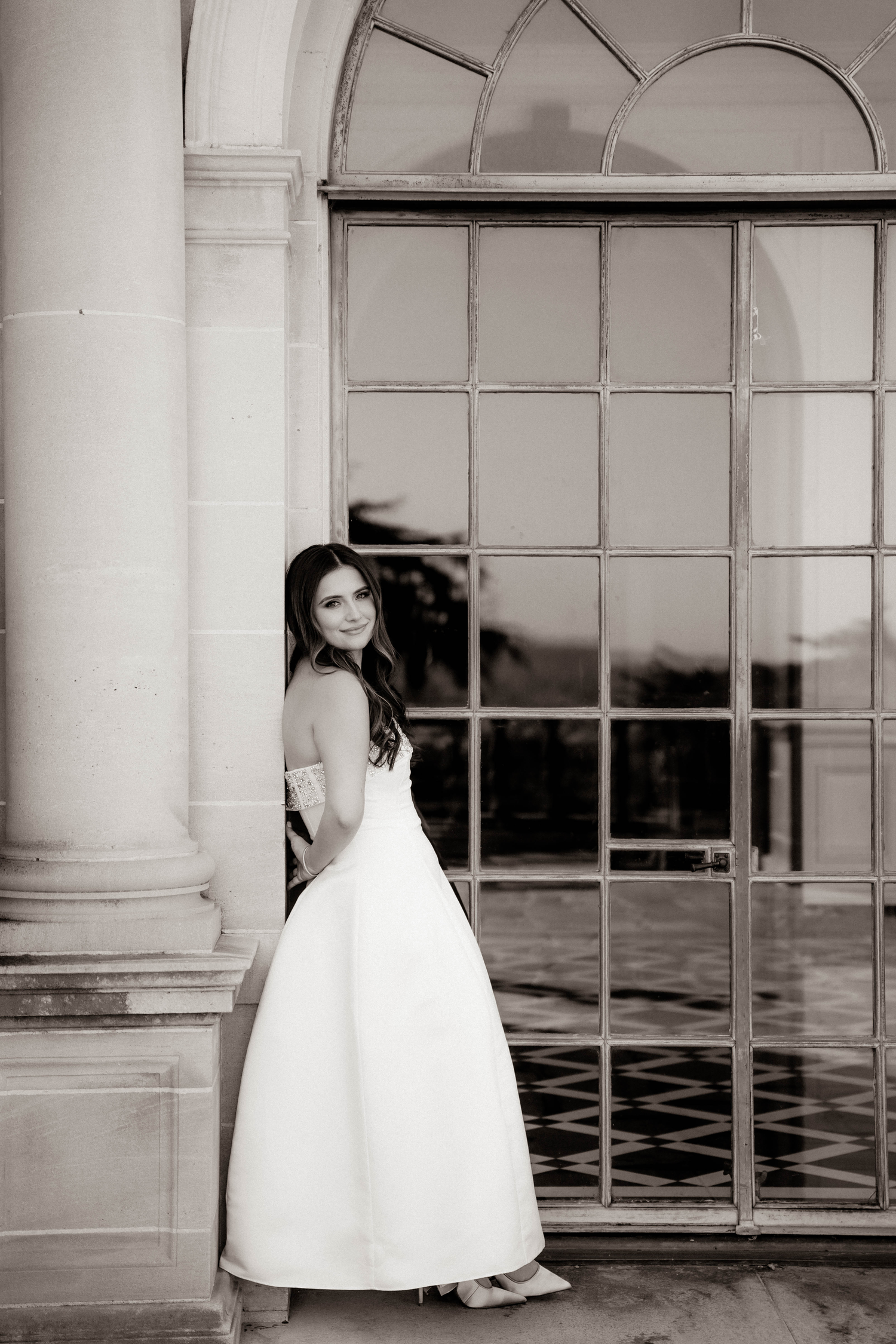 Elegant bride in strapless white ball gown poses by arched window in black and white portrait. Greystone Mansion & Gardens