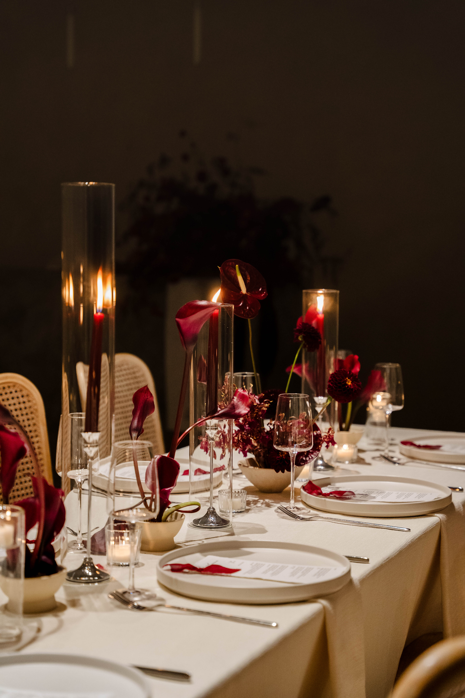 Elegant wedding reception table set with tall glass candles, red roses, wine glasses, and cream linen.