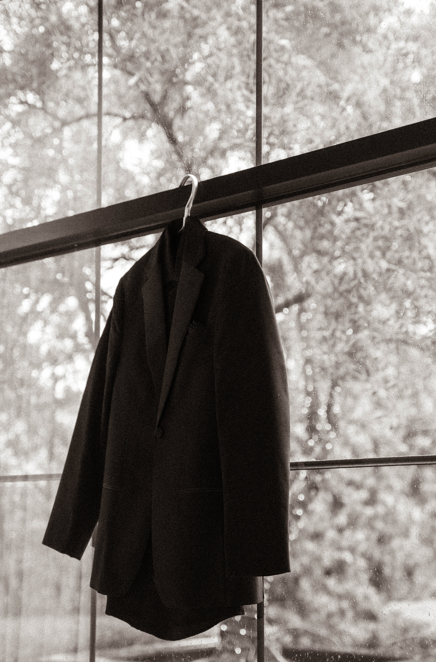 Black blazer hanging on a metal rod against a large window with trees visible in the background.