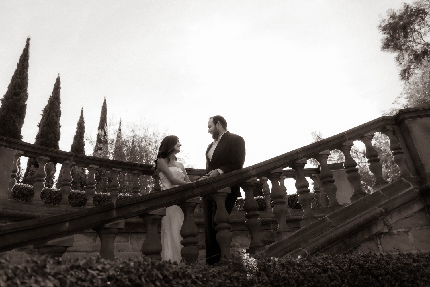 Dramatic black and white photo of an elegant couple on ornate stone stairs at dusk.