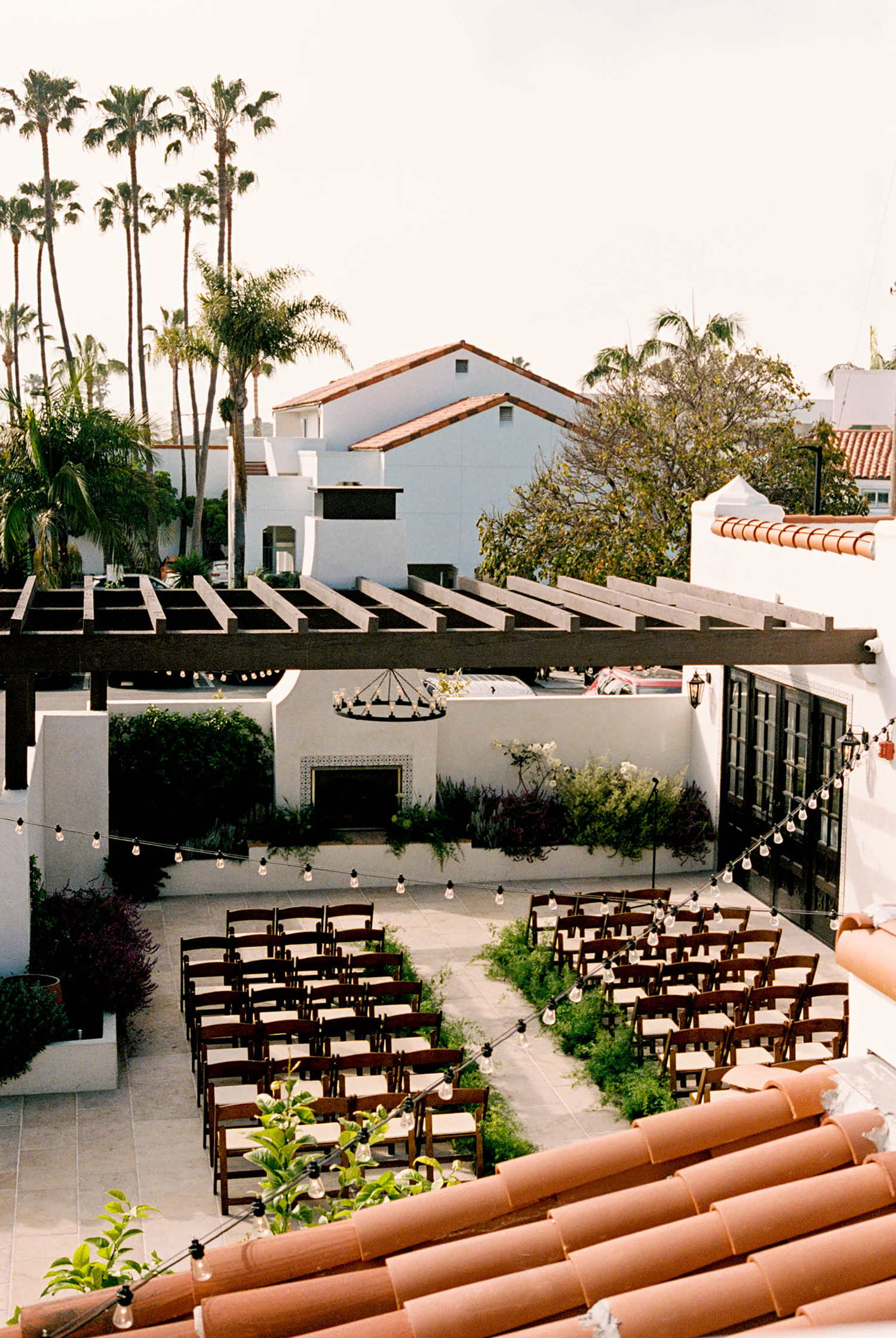 Aerial view of an elegant outdoor wedding ceremony setup with wooden chairs in a Spanish-style courtyard with palm trees.