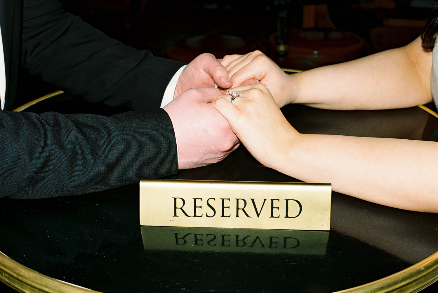 Couple holding hands over a reserved sign on a black table, suggesting a romantic dinner reservation.