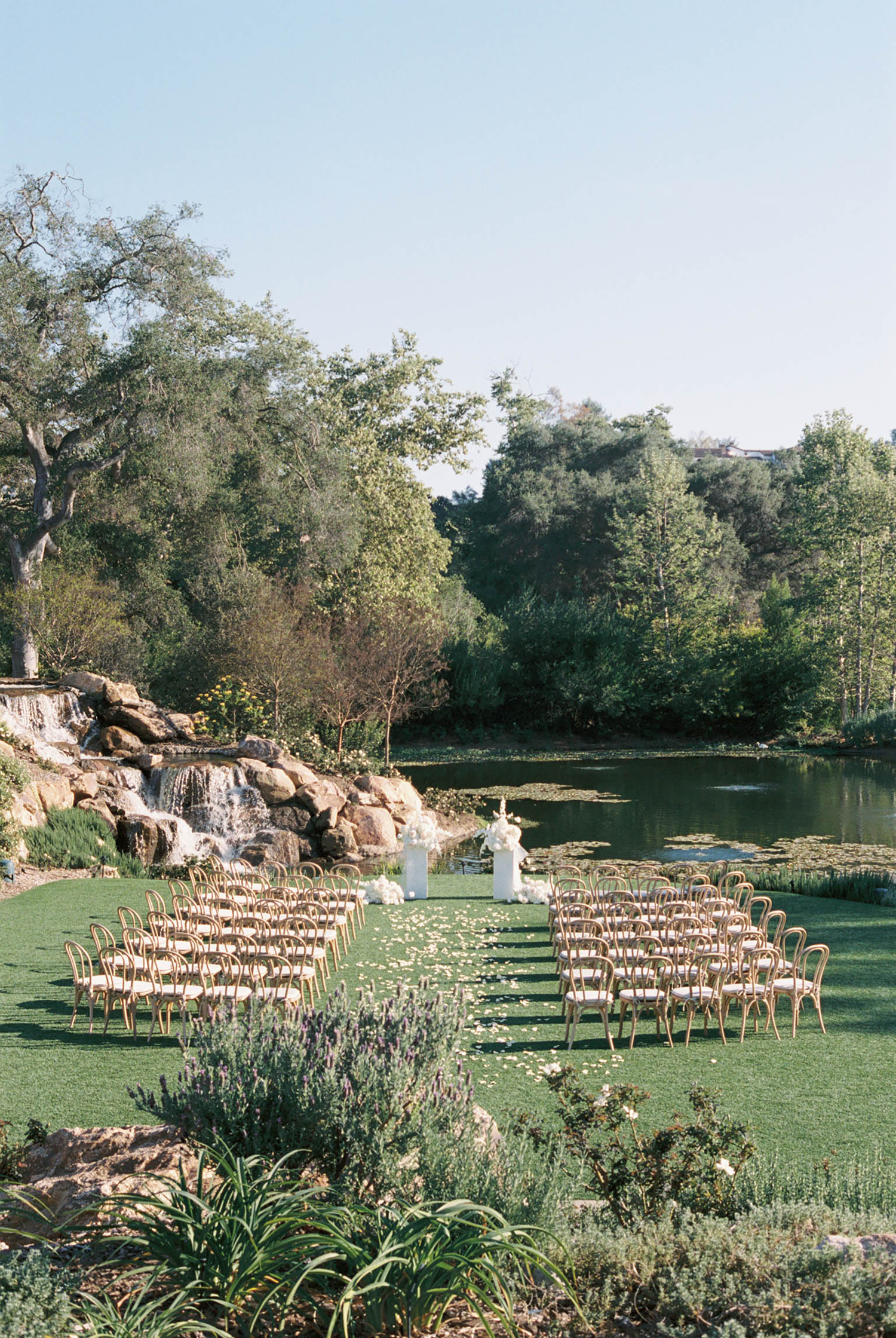 Elegant outdoor wedding ceremony setup with rows of chairs beside a tranquil pond.