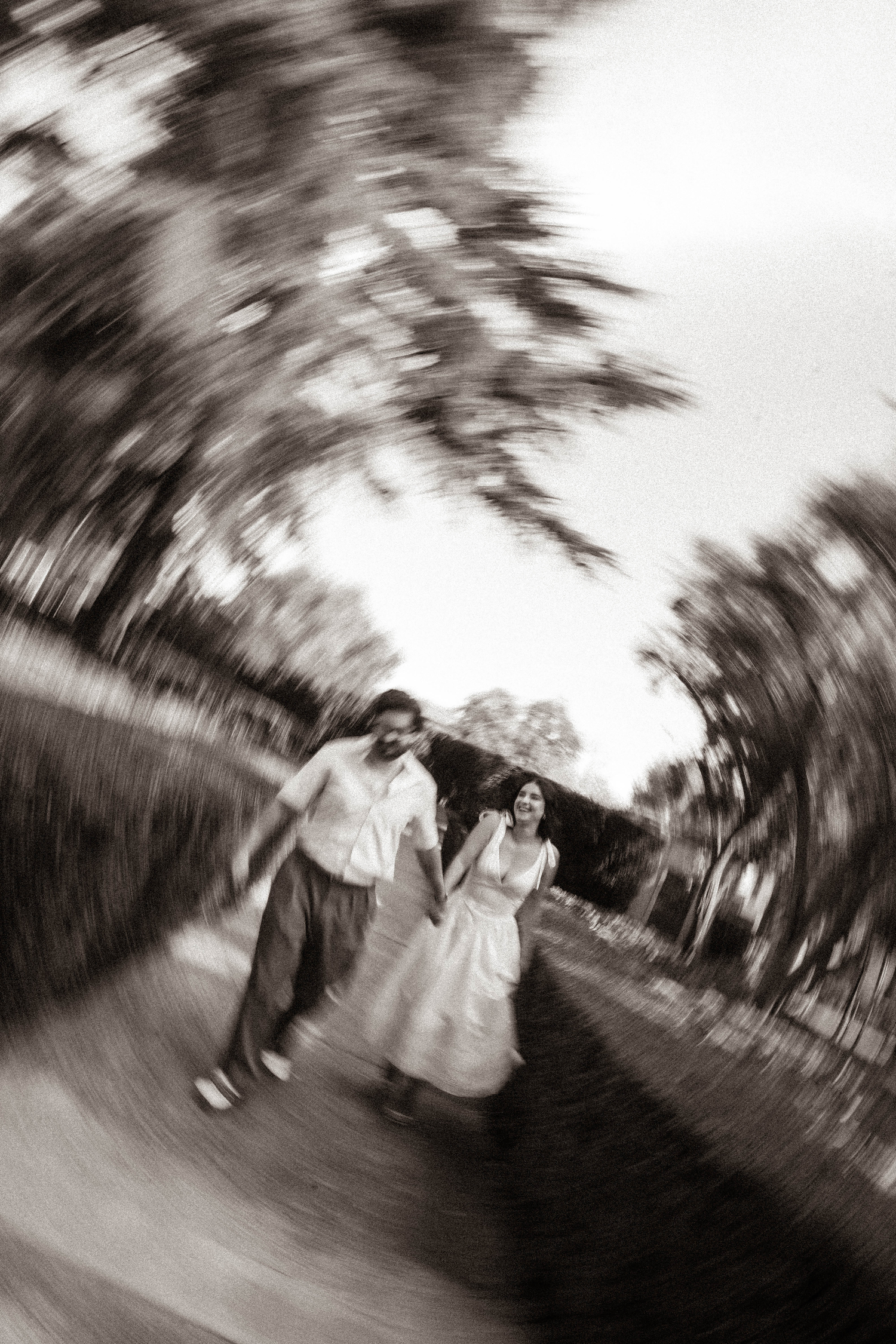 Black and white swirling motion blur photo of couple laughing and running outdoors together.
