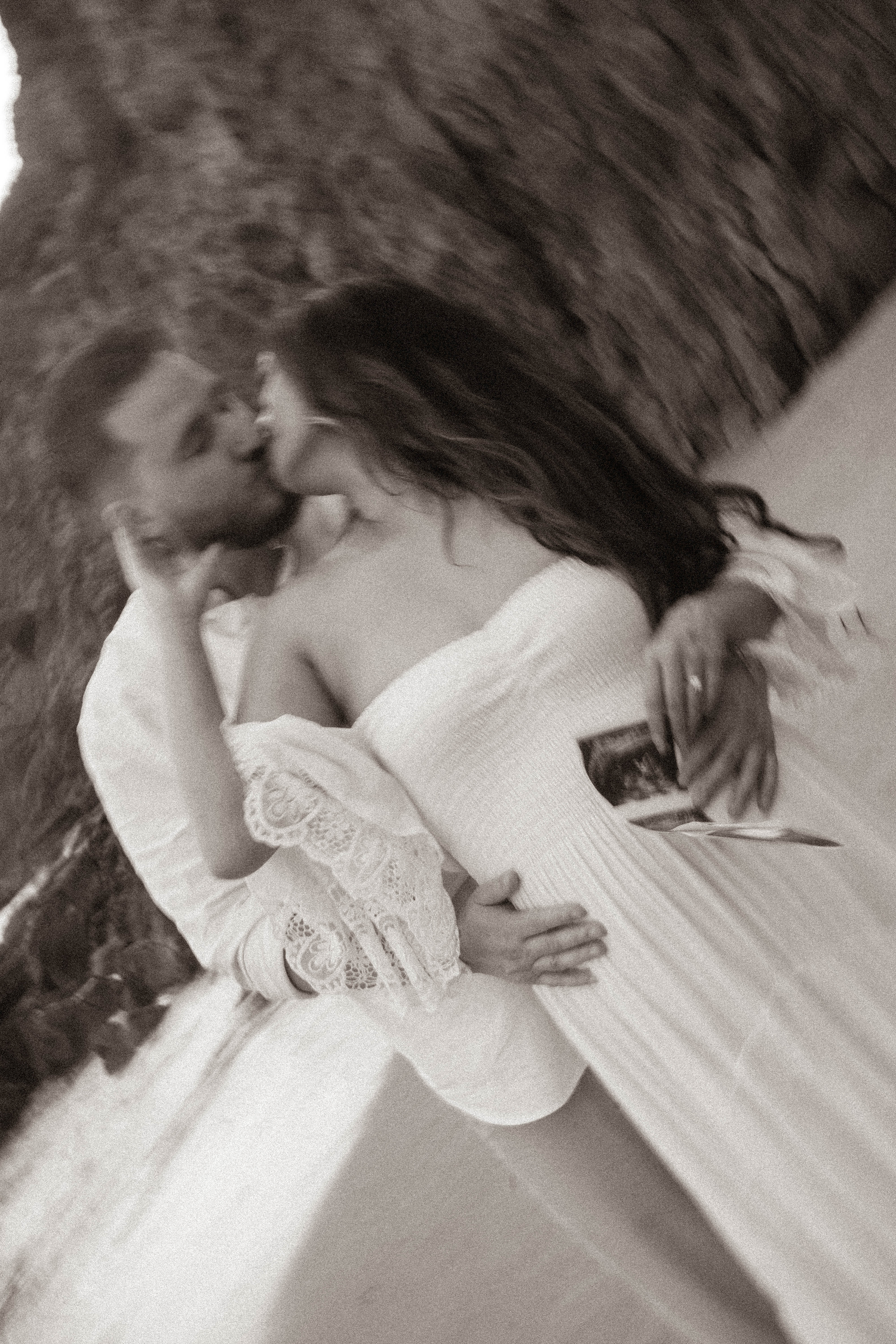Black and white photo of pregnant couple kissing near rocky cliffs, maternity session.
