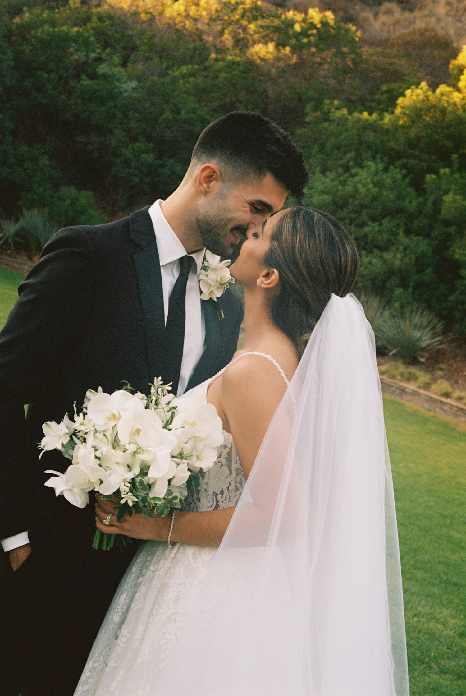 Bride and groom sharing an intimate forehead touch moment outdoors, bride holding white floral bouquet in wedding attire.