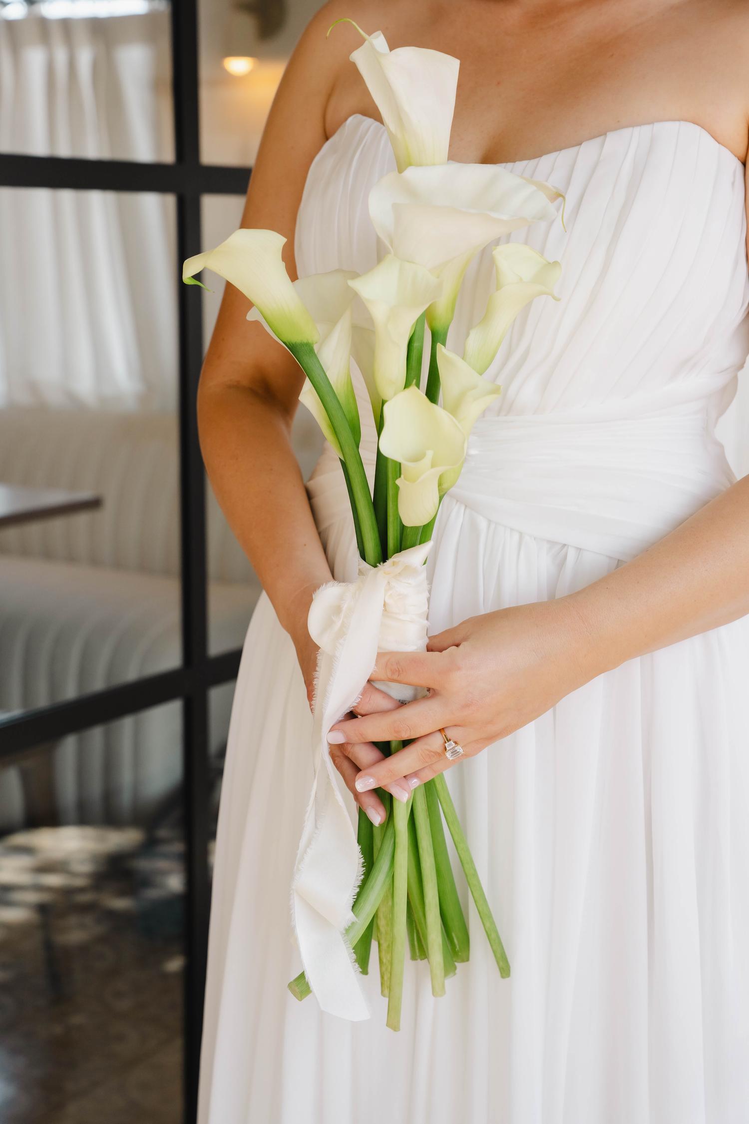 Bride holding an elegant bouquet of white calla lilies tied with a satin ribbon in a strapless wedding gown.
