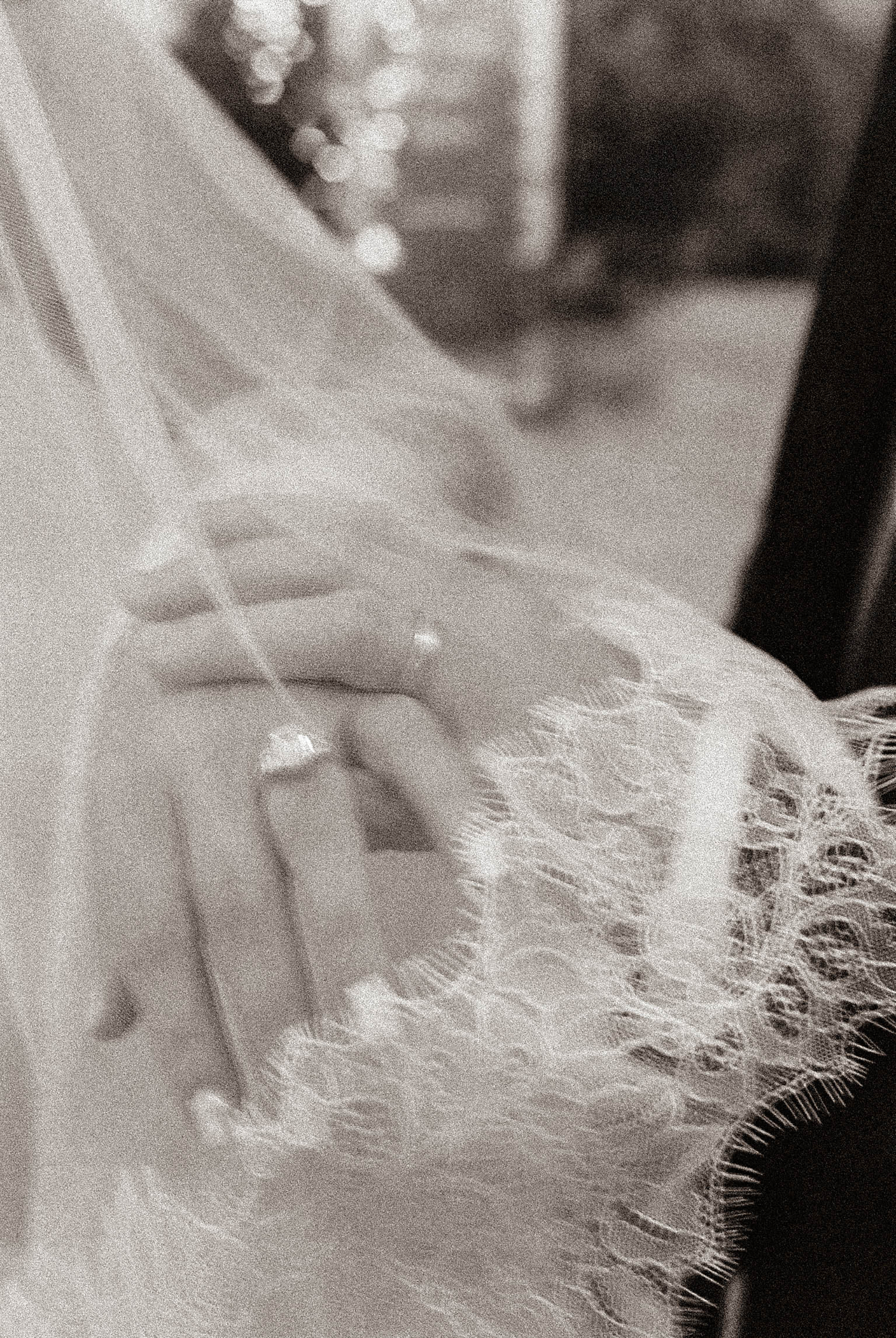 Black and white photo of a bride's hands showing wedding ring, wearing lace dress and veil.