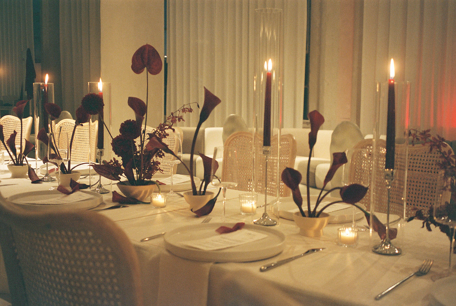 Elegant formal dining table set with black candles, white calla lilies, and glowing votives for a sophisticated event.