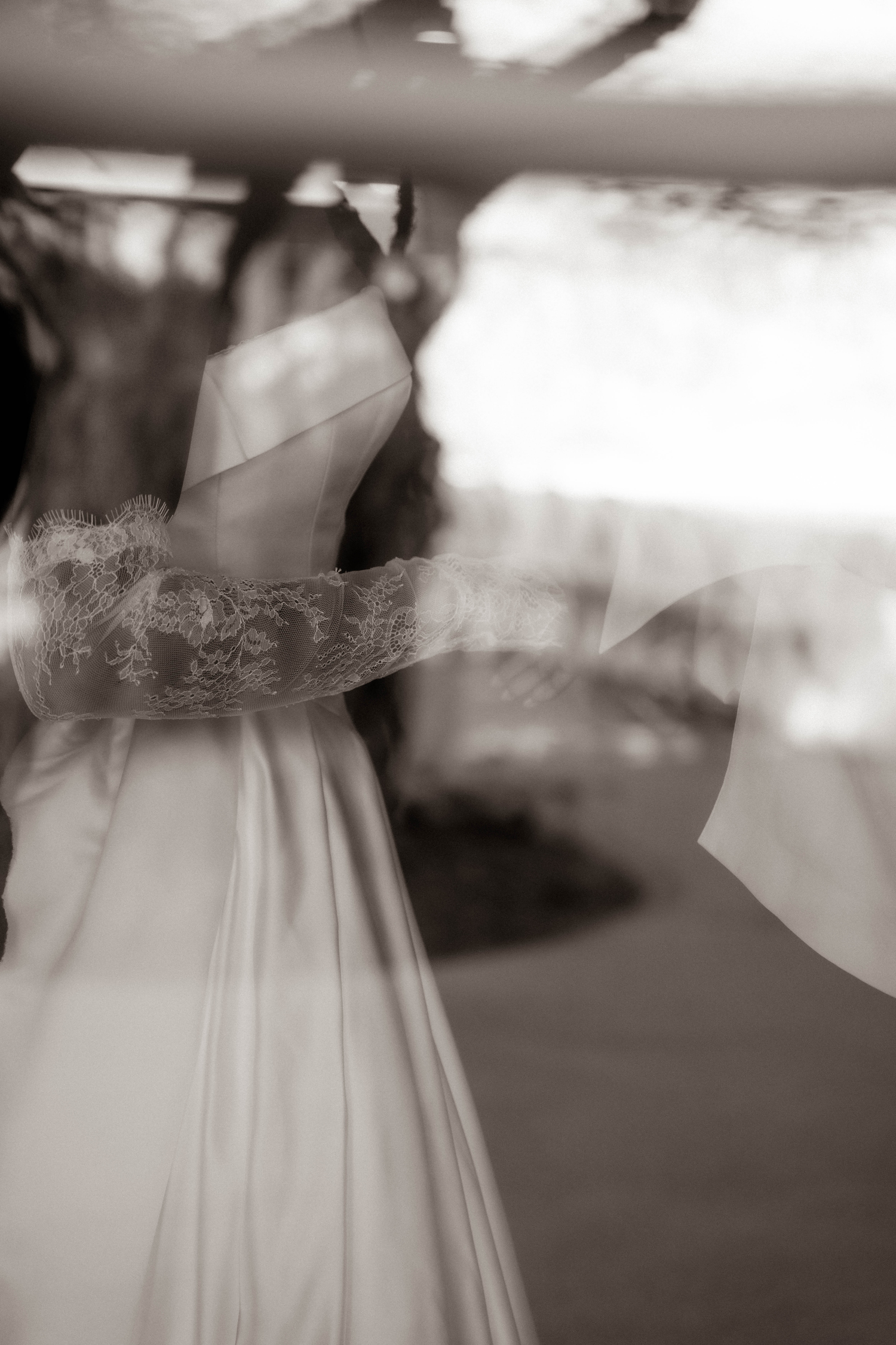 Black and white photo of a bride in a lace wedding dress with flowing veil outdoors.